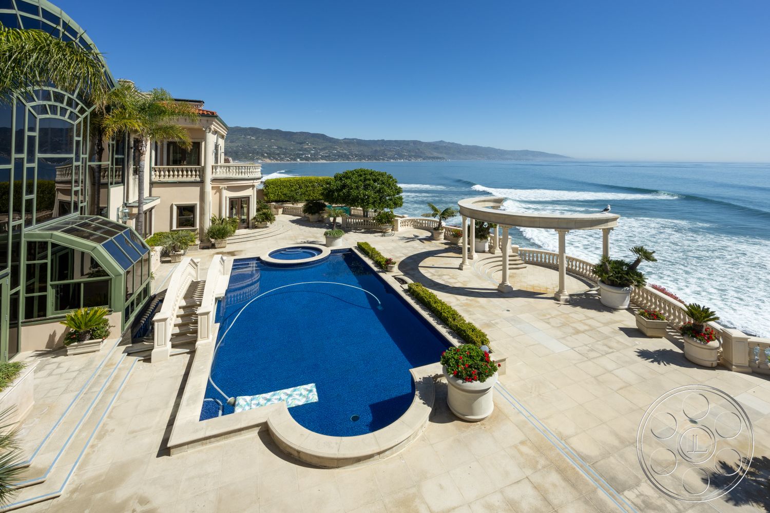 Pacifica Estate - rectangular swimming pool, outdoor dining area, modern architectural style, coastal setting, sunny outdoor space, oceanfront view, sandy beach access, wooden pergola structure, exterior concrete patio flooring, balcony with ocean view, landscaped garden with palm trees, curved swimming pool edge, hardscaped patio area, potted plants for landscaping, exterior tiled pool deck, glass wall garden feature, exterior stone wall accents, luxury beachfront property, exterior stone columns, infinity pool design, stylish outdoor lounge area