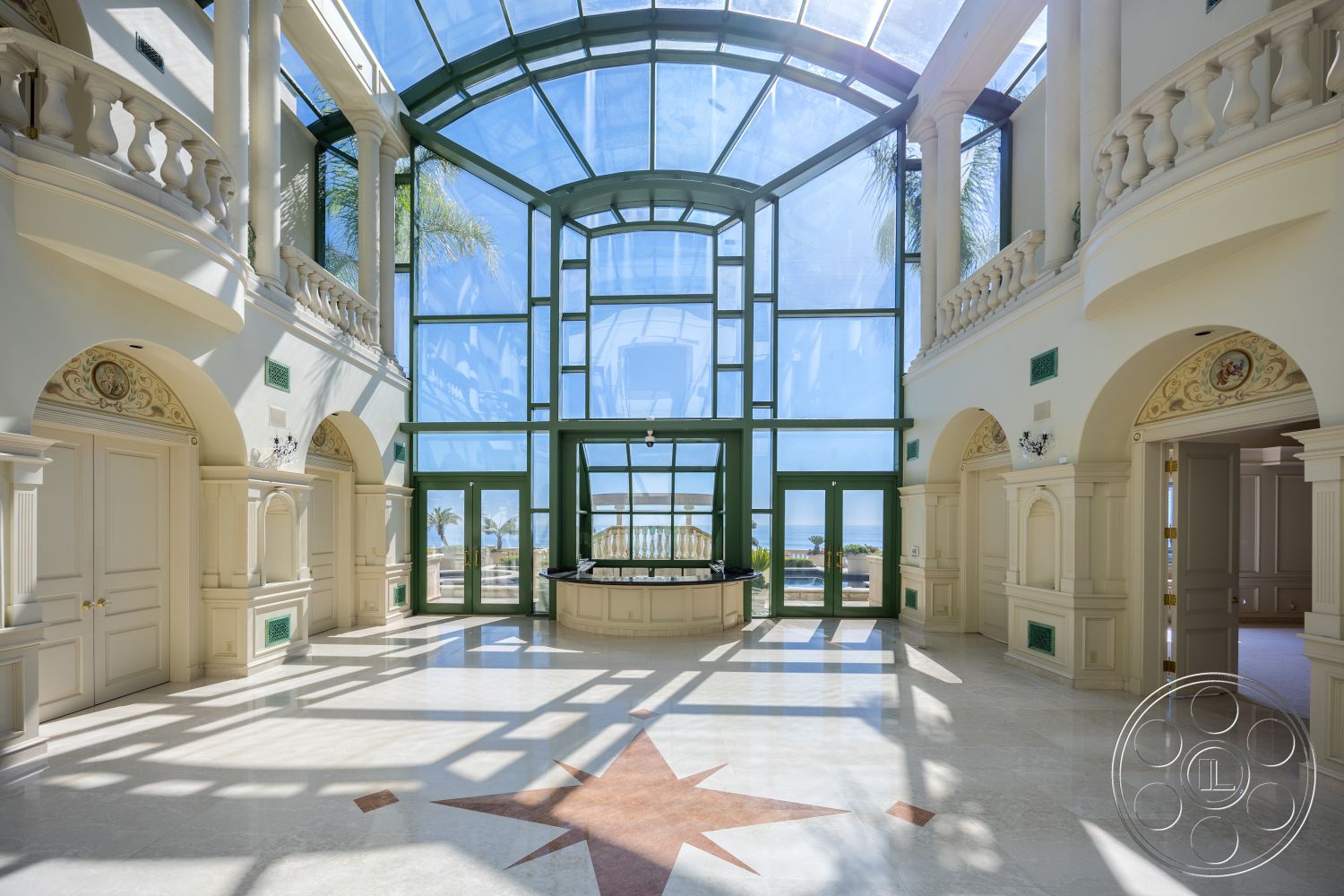 Pacifica Estate - resort, palm tree view, large floor-to-ceiling windows, open floor plan layout, elegant chandelier lighting, interior marble flooring, decorative wall moldings, glass wall structure, arched entryway details, ornate ceiling with skylight, columned design features, coffered ceiling accents, intricate star pattern inlay, green and white color scheme, luxurious foyer space, palatial architectural style, oceanfront property access