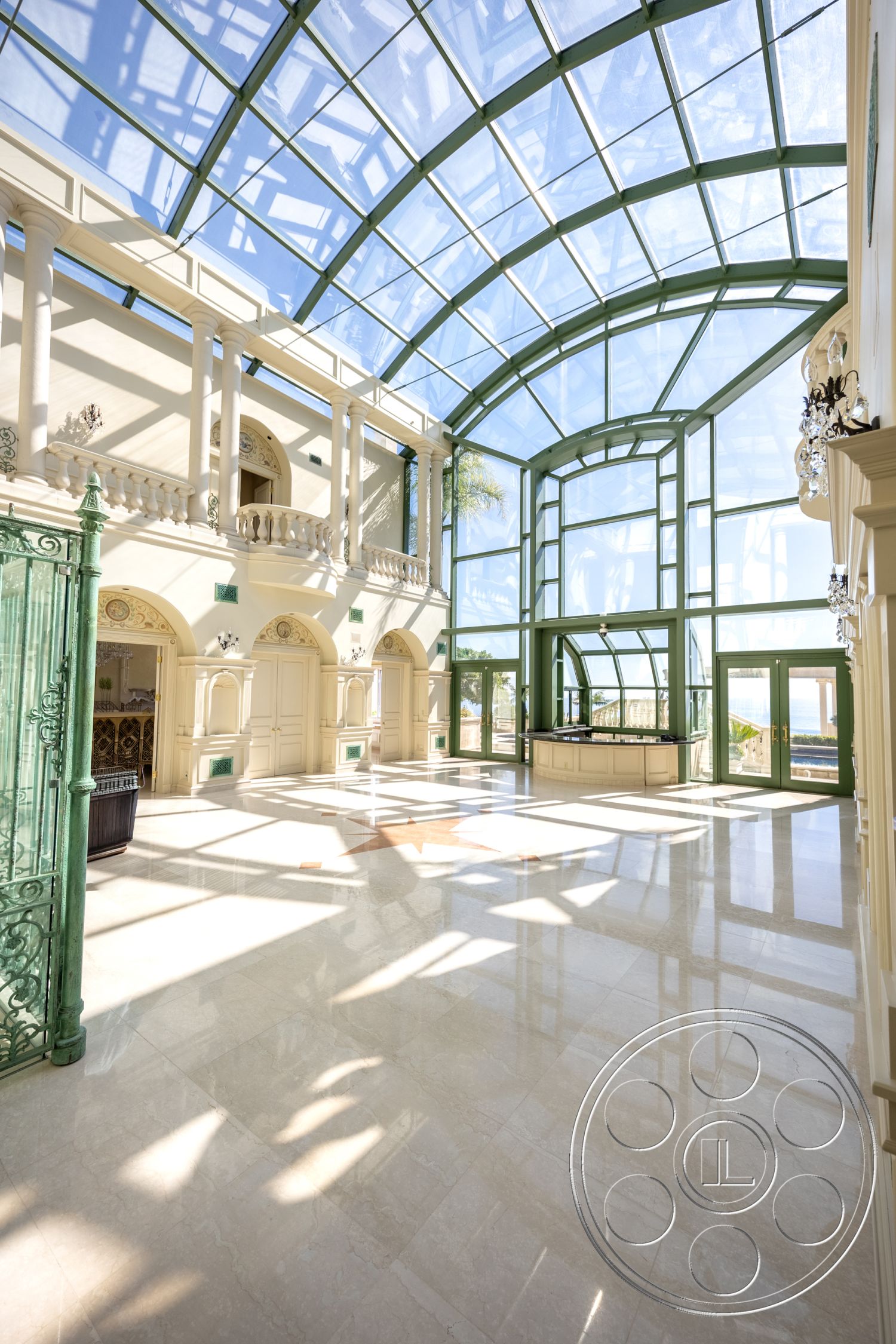Pacifica Estate - natural lighting, marble flooring, luxurious atmosphere, exposed steel beams, open-concept space, ornate balcony railing, intricate molding details, plaster wall finishes, glass vaulted ceiling, green painted window frames, elegant lobby design