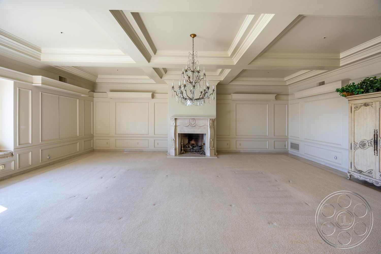 Pacifica Estate - neutral color palette, textured plaster walls, exposed wood ceiling beams, interior living room, open floor plan layout, soft natural light from windows, crown molding ceiling details, chandelier lighting fixture, traditional fireplace surround, cream carpet flooring, built-in cabinetry with intricate details, panelled wall treatments