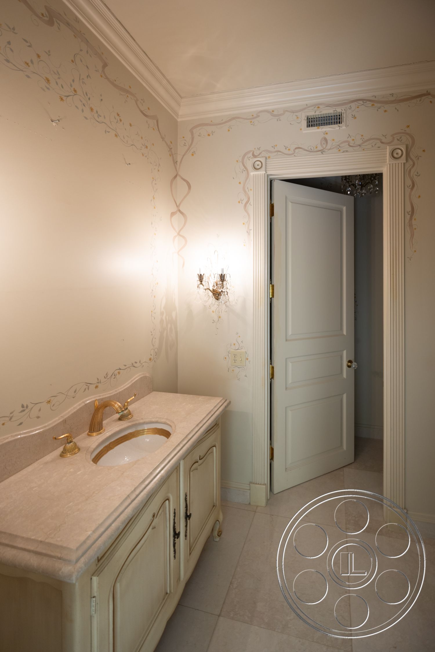 Pacifica Estate - neutral color palette, decorative crown molding, interior bathroom, tile bathroom flooring, minimalist decorative elements, marble vanity countertop, white paneled door, cream-colored cabinetry, dual gold faucet sinks, intricate painted wall details, elegant wall sconce lighting, stylish door trim