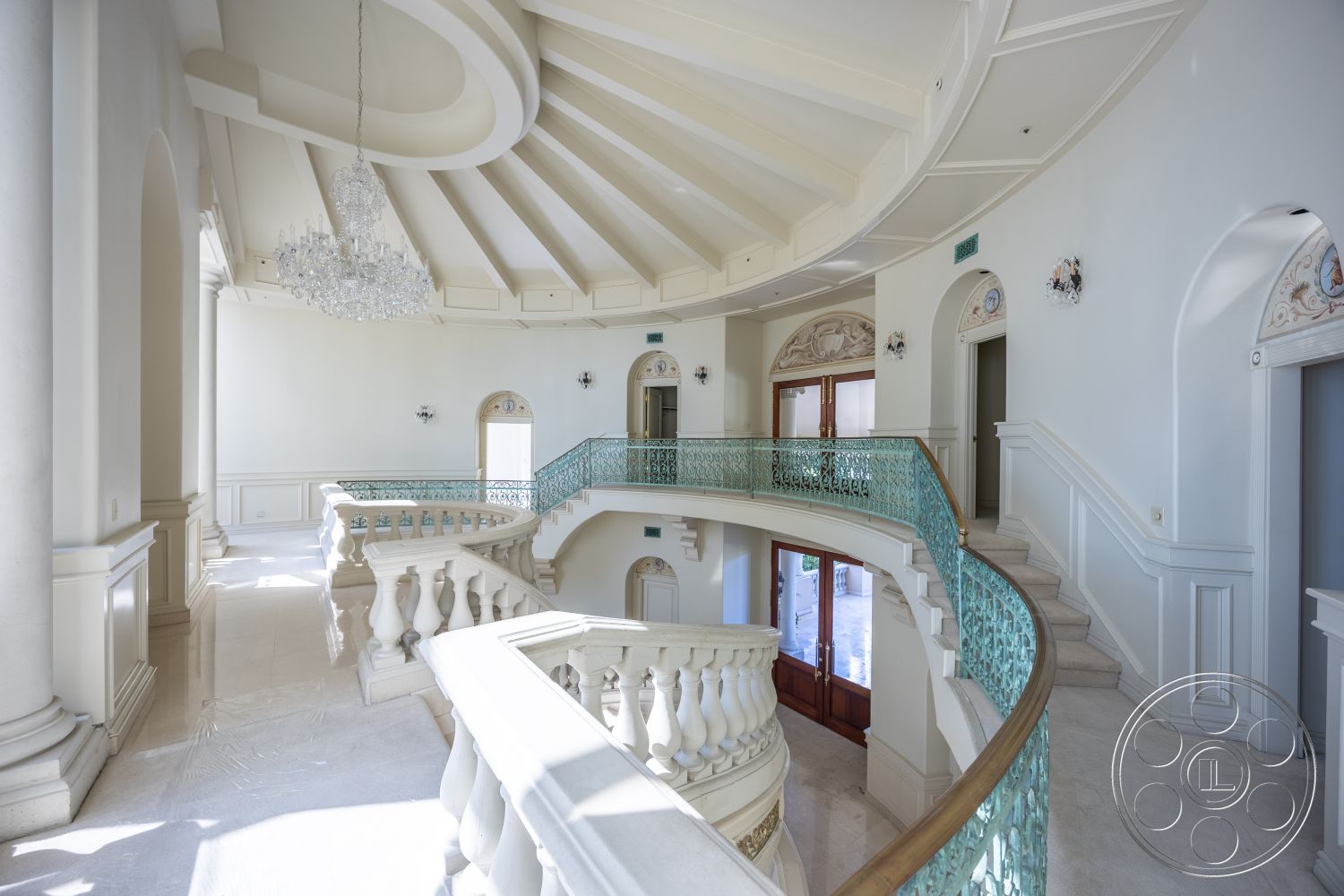 Pacifica Estate - coffered ceiling, crystal chandelier, marble flooring, arched doorways, luxurious entryway, elegant architectural details, decorative wall paneling, glass partition walls, recessed lighting fixtures, white painted walls, wrought iron balcony railing, expansive open space, round staircase, natural light floods, intricate cornice moldings