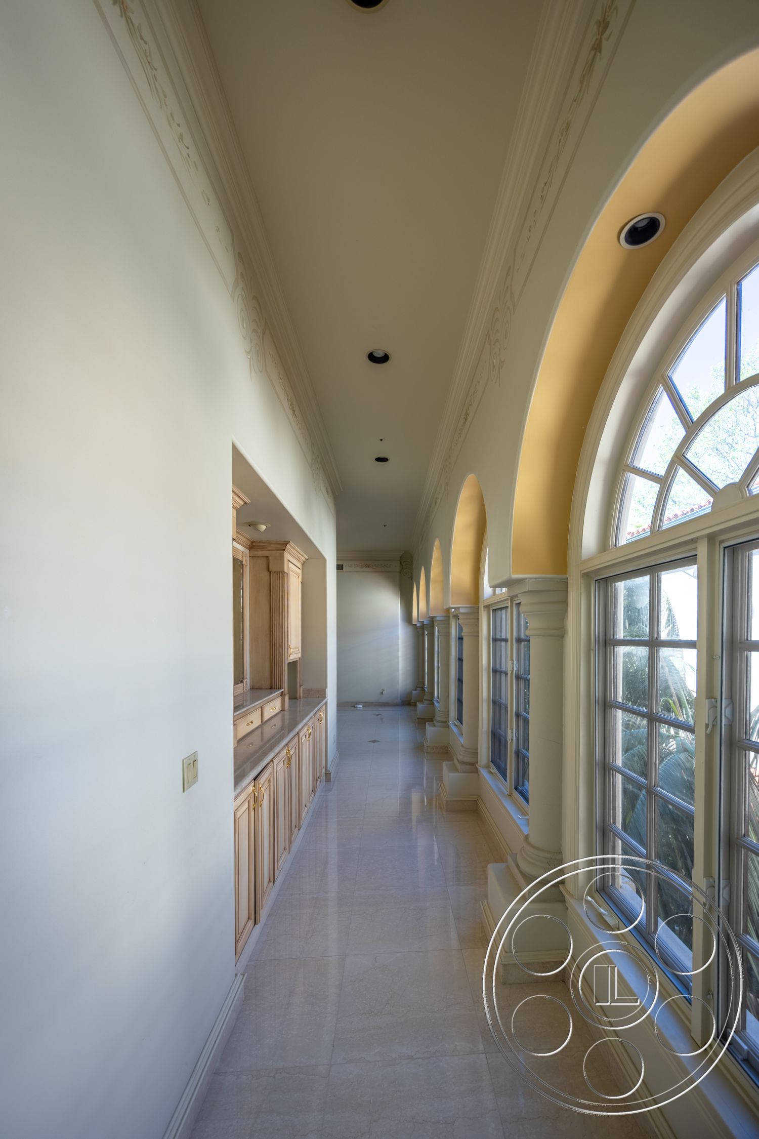 Pacifica Estate - interior recessed lighting fixtures, interior large glass windows, interior crown molding details, interior marble hallway flooring, interior wooden cabinetry with natural finish, interior arched windows with mullion design, interior high ceilings with decorative plaster, interior stone column supports, interior light-colored painted walls, interior elegant corridor design, interior smooth ceiling with decorative elements