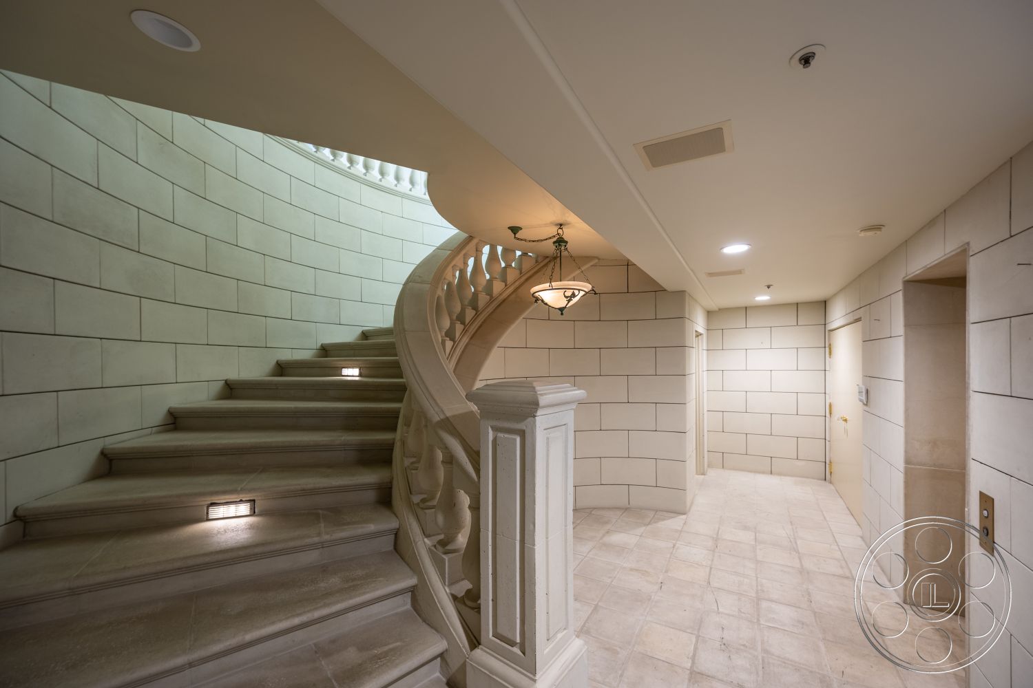 Pacifica Estate - textured stone wall, natural light from skylight, ambient recessed lighting, modern elevator access, neutral color palette walls, marble flooring in entryway, spacious landing area, coffered ceiling detail, curved staircase with decorative railing, luxurious interior design, transitional style architecture, exterior stone staircase, architectural pendant lighting, open-concept foyer, elegant archway leading to hall, solid core door finishes, polished stone tile floors, intricate ornamental railing, high-end materials used throughout, stylized wall sconce lighting