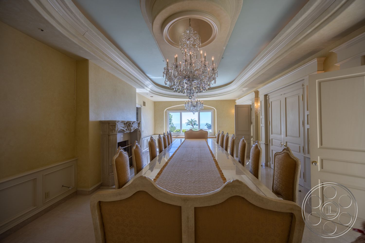 Pacifica Estate - marble flooring, arched doorways, curved wall design, spacious dining area, elegant table setting, natural light flooding in, oceanfront view, interior coffered ceiling, cream painted walls, exterior glass windows, traditional dining room, exposed decorative ceiling, luxurious chandelier lighting, high-backed upholstered chairs, fluted column details, built-in fireplace surround