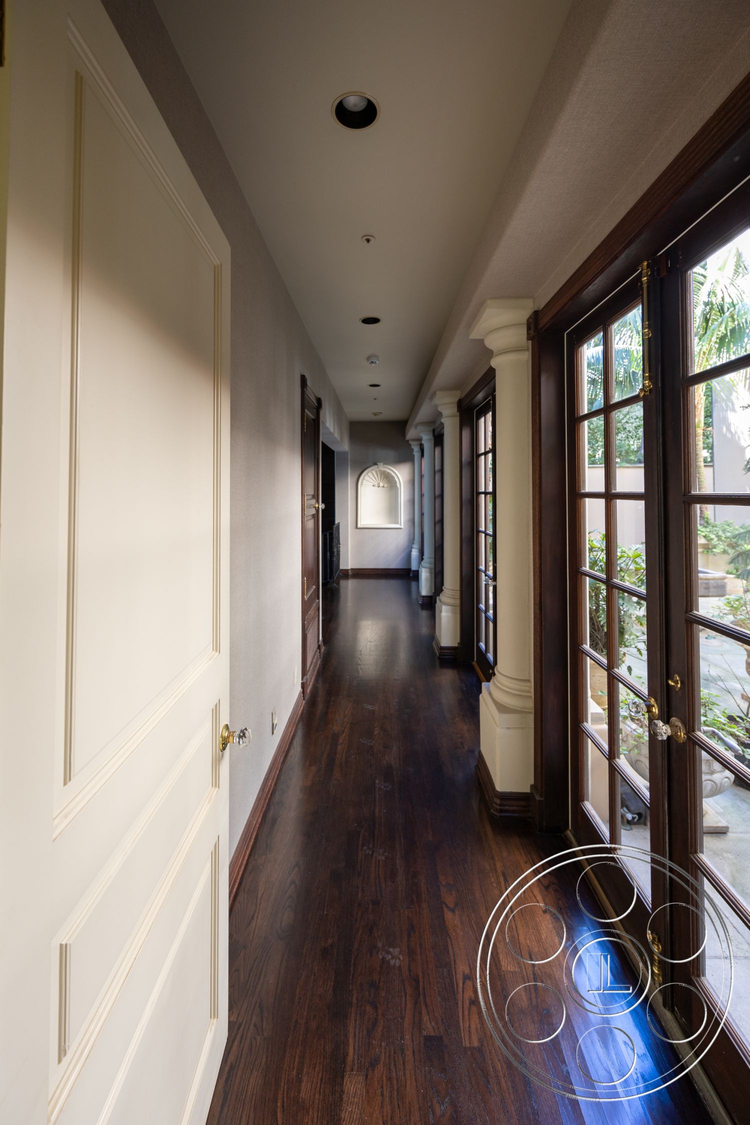 Pacifica Estate - recessed ceiling lights, transom windows above doors, decorative crown molding details, natural light from exterior, hardwood hallway flooring, interior corridor with French doors, neutral textured plaster walls, traditional style wood trim, arched wall niche, elegant door hardware, spacious linear hallway, classic interior design elements