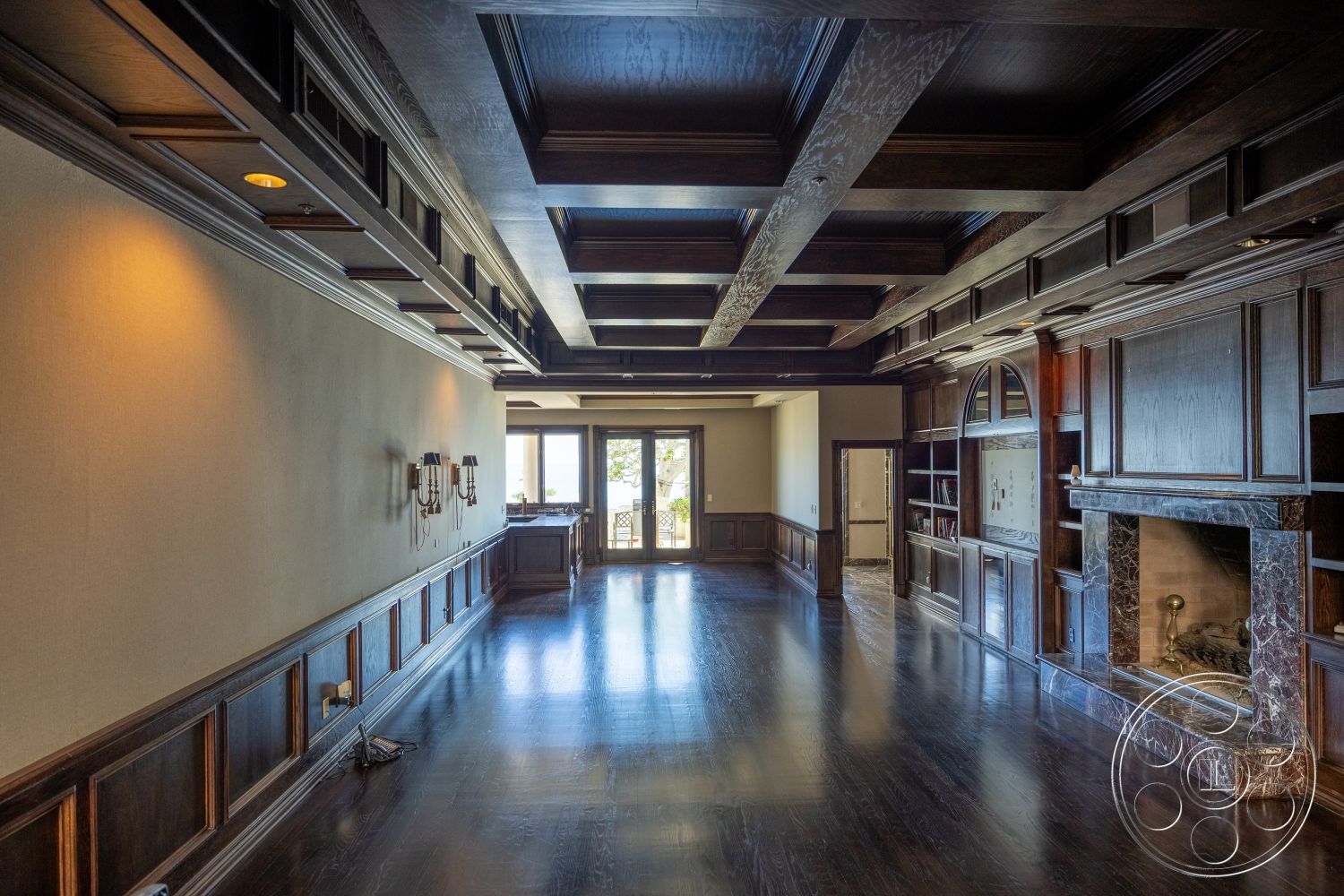 Pacifica Estate - open floor plan, warm color palette, floor-to-ceiling windows, arched doorways, textured plaster walls, modern rustic style, dark wood paneling, exposed ceiling beams, luxurious interior, built-in bookshelves, hardwood living room floors, natural light emphasis, marble fireplace surround, coffered wood ceiling, plush wall sconces, formal living room, elegant gathering space, breathtaking view access, sophisticated architectural details