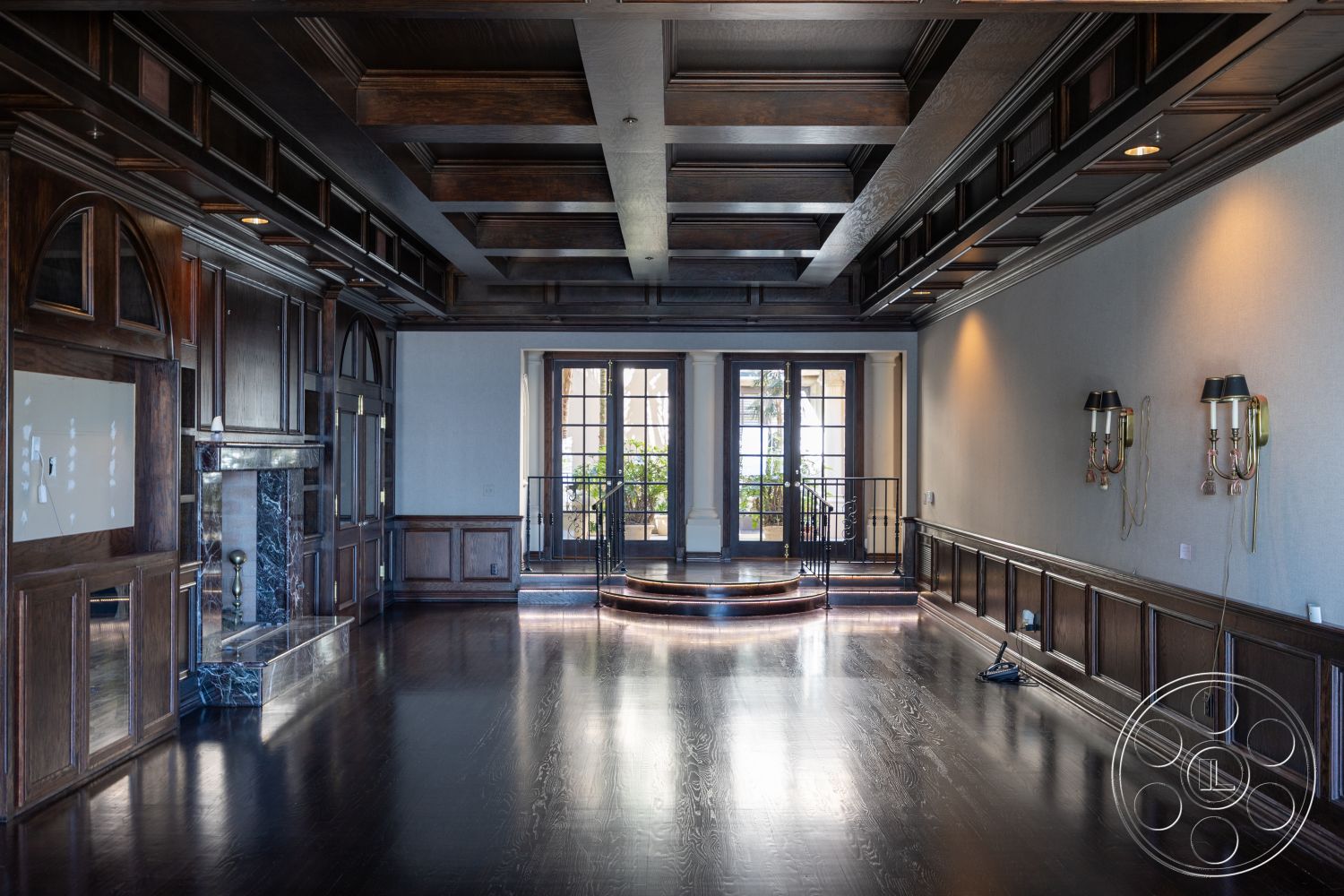 Pacifica Estate - hardwood floor, ornate wall sconces, traditional design elements, exposed wood trim details, interior lounge area, high-end interior finishes, glass French doors, curved staircase with wrought iron railings, exterior wooden wall paneling, dark wood coffered ceiling, black marble fireplace surround, elegant architectural molding, large windows with arched tops, luxurious residential space, spacious open living area, well-lit entertainment space