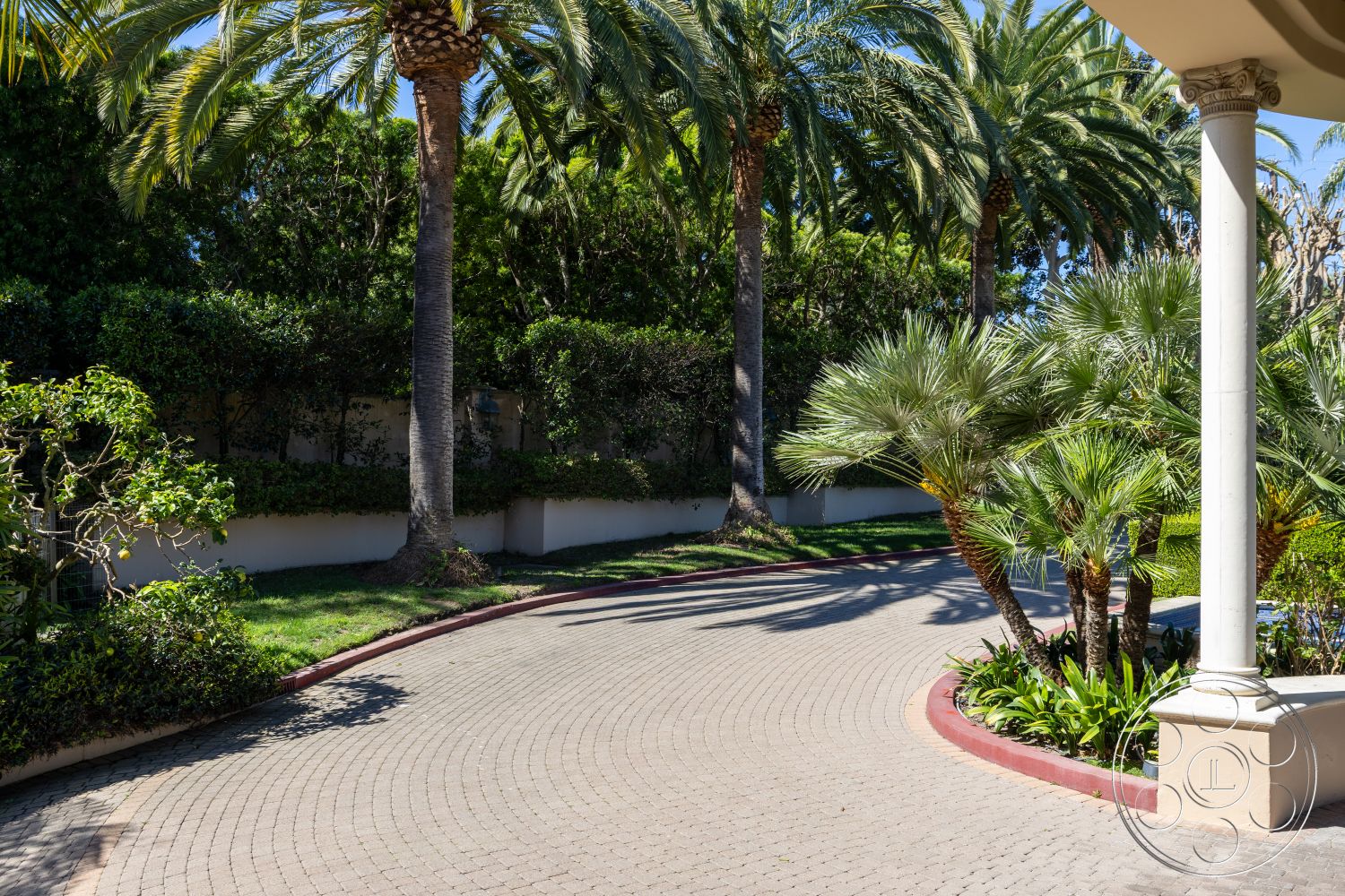 Pacifica Estate - palm trees, tropical landscaping, lush green hedges, well-manicured lawn, modern architectural details, brick driveway pavers, desert climate setting, exterior stone wall, curved driveway entrance, paved circular driveway, bordered flowerbeds