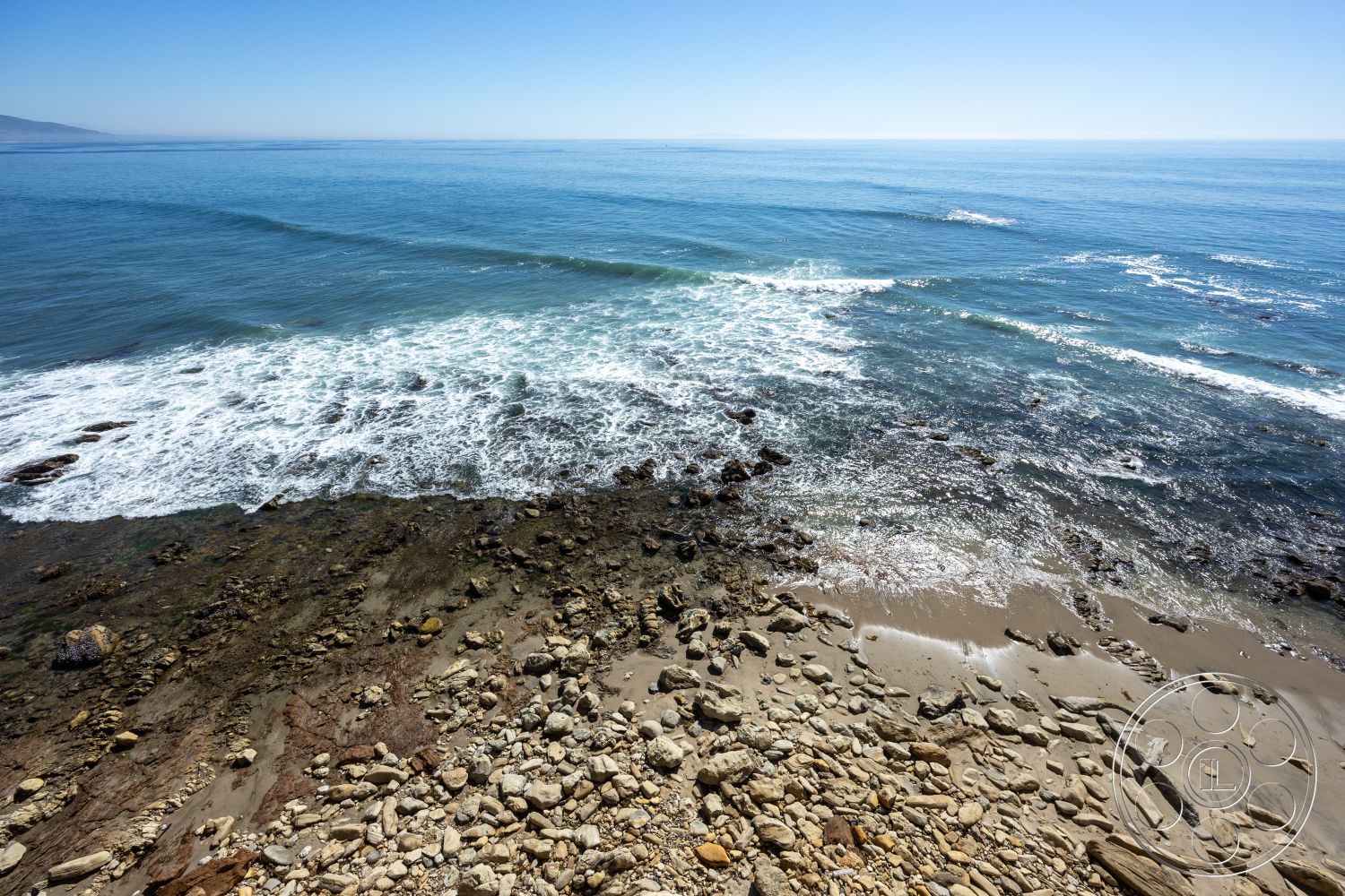 Pacifica Estate - clear blue sky, coastal landscape, rocky coastline, ocean waves, sunny outdoor space, scenic ocean view, sandy beach area, beachfront environment, natural stone beach, marine setting, tidal zone, marine rocks, wet sand patterns, seaside boulders, driftwood elements, tropical climate, tranquil waterscape