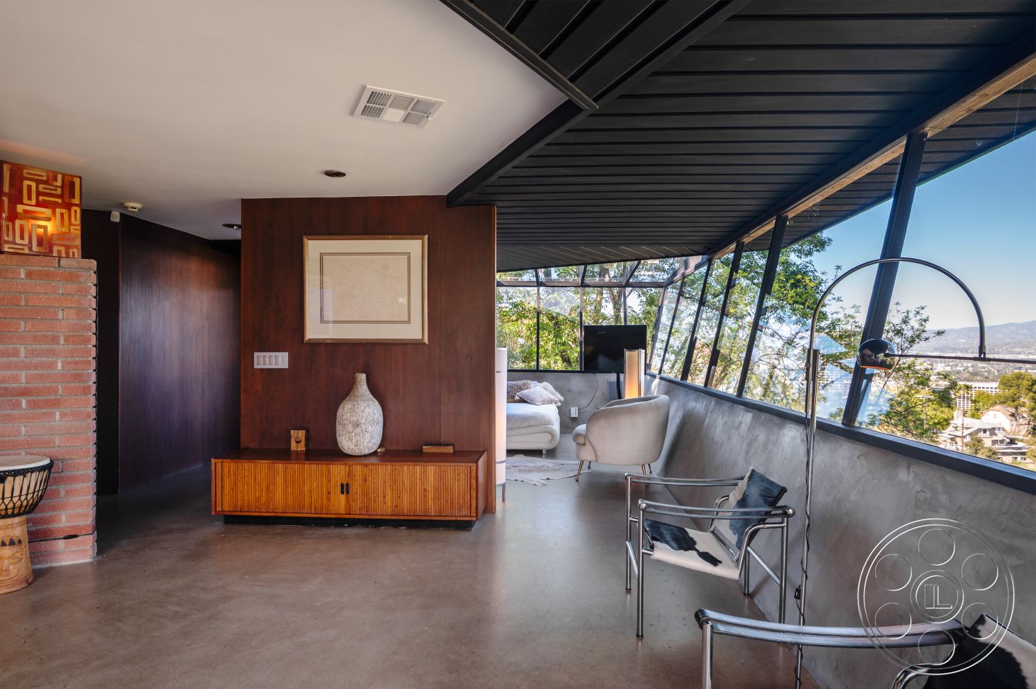 Retro 31 - floor-to-ceiling windows, dark wood paneling, mid-century modern architecture, brick fireplace surround, natural light-filled space, contemporary art decor, open floor plan layout, minimalist furniture design, interior polished concrete floor, exterior glass wall, surrounding hillside view, functional living space, angled roof overhang, wood veneer sideboard, urban mountain retreat