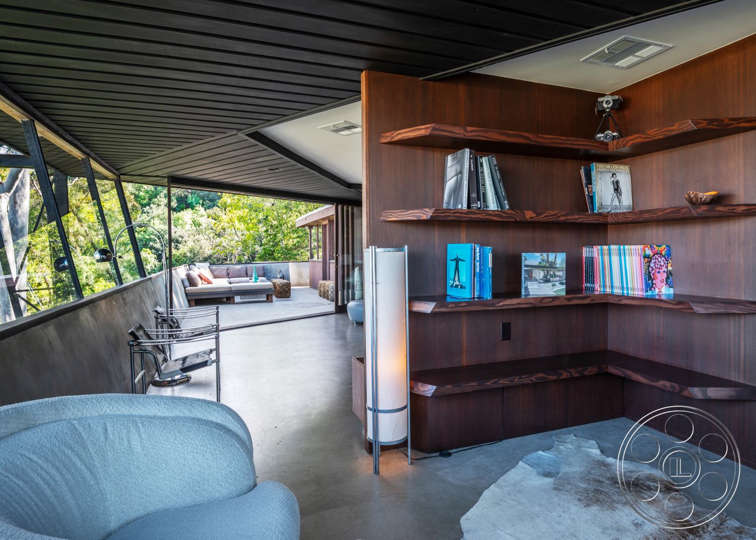 Retro 31 - concrete flooring, minimalist design elements, warm wood tones, floor-to-ceiling windows, textured wall treatment, modern light fixture, outdoor patio view, exposed wood ceiling beams, integrated seating area, natural light infiltration, glass wall partition, interior lounge area, urban environment setting, surrounding greenery view, polished concrete surface, curved bookshelves, contemporary open floor plan, wood veneer shelving, private home office area, cohesive indoor-outdoor flow