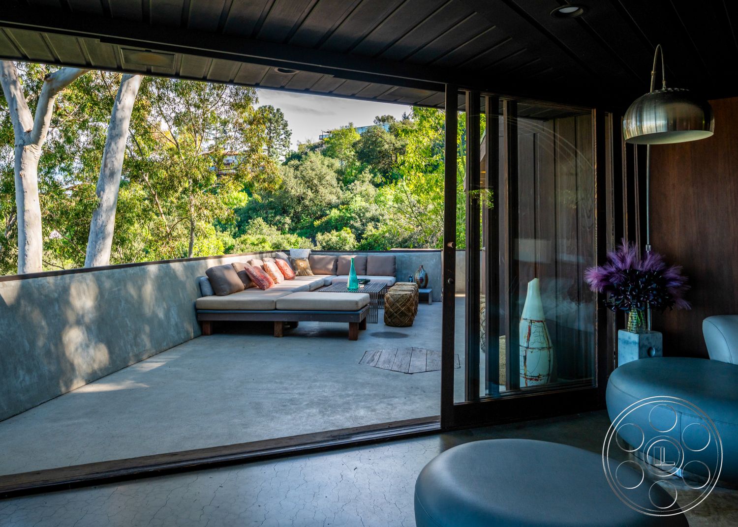 Retro 31 - exterior concrete patio floor, open-concept outdoor living space, interior floor-to-ceiling glass doors, contemporary outdoor lounge area, exterior landscaped surroundings, minimalist furniture arrangement, interior ambient lighting fixtures, interior modern furniture design, interior wooden accent wall, interior monochromatic color scheme, exterior wooden railing, interior decorative vases, exterior concrete wall with smooth finish, exterior curved balcony, interior seating arrangement with sectional sofa, exterior natural greenery view, ceiling with dark wood paneling, interior round decorative table, stone-like exterior wall treatment, exterior natural light infiltration