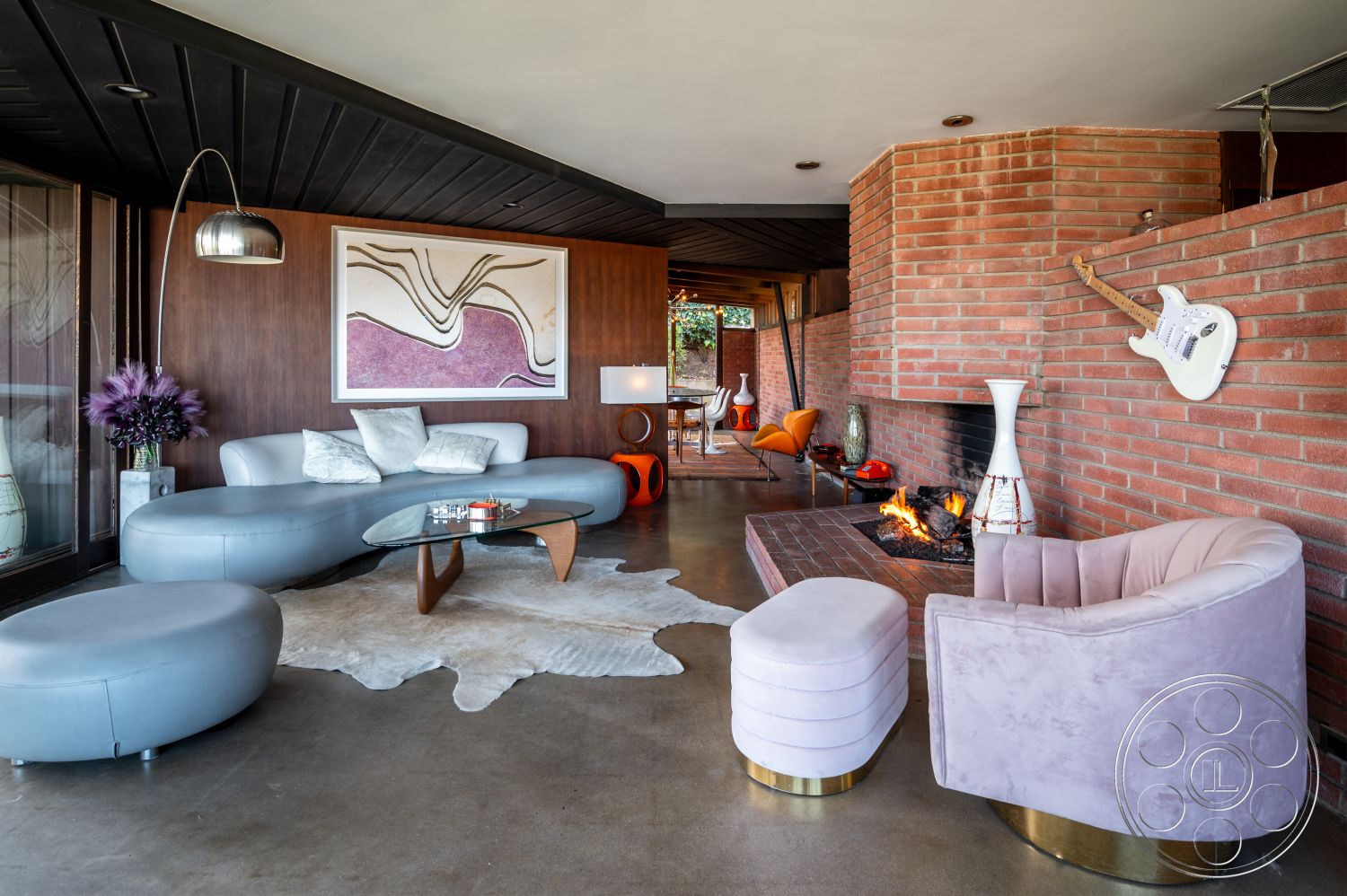 Retro 31 - cozy seating arrangement, floor-to-ceiling windows, exposed wood ceiling beams, interior brick fireplace surround, garden view setting, interior patterned area rug, curved furniture shapes, interior wood paneling wall, interior modern art wall decor, interior concrete floor treatment, interior leather curved sofa, interior round glass coffee table, interior vinyl lounge chair, interior plush velvet armchair, interior cowhide rug, exterior patio door access, two-story open living space, modern mid-century architectural style, wood accent wall treatments, ambient fire feature