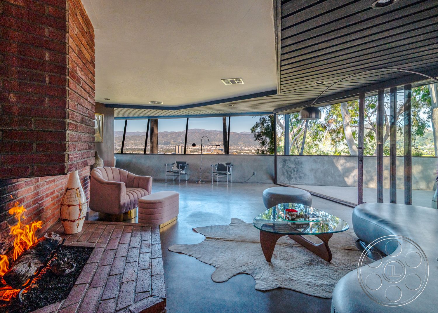 Retro 31 - polished concrete flooring, interior living space, mid-century modern architectural style, exposed brick fireplace surround, vaulted ceiling with wooden beams, neutral-toned area rug, floor-to-ceiling windows with city view, open-concept interior layout, suburban hillside location, contemporary glass coffee table, curved sectional sofa in living room, steel and wood dining chairs, natural light from panoramic windows, modern art on display