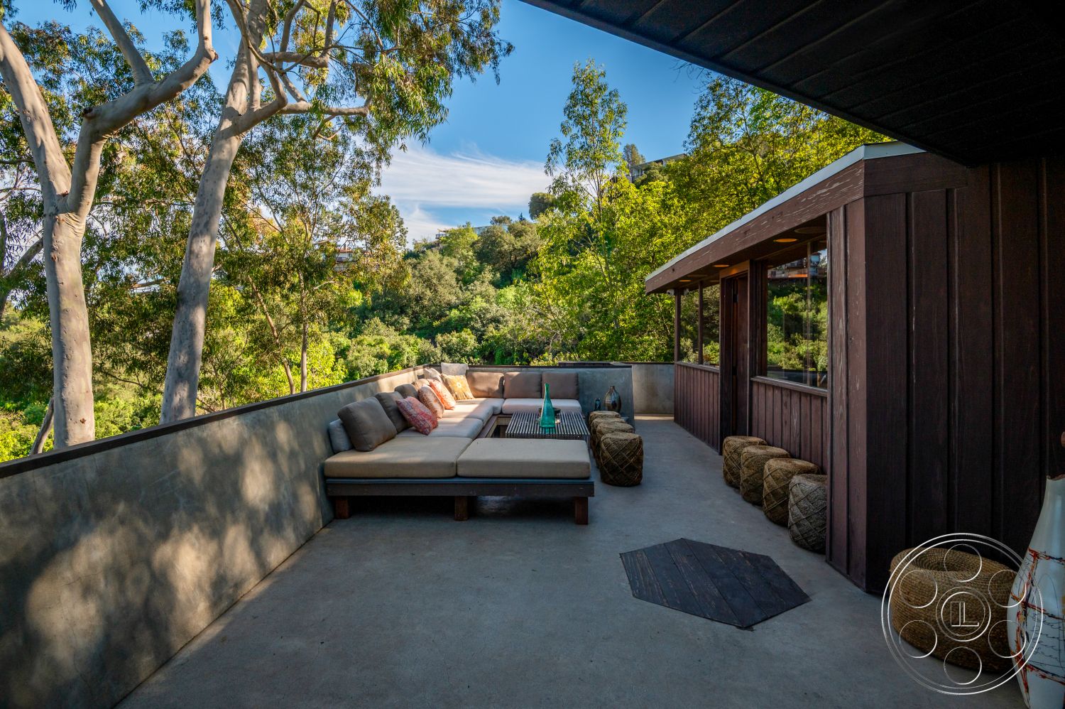 Retro 31 - surrounding greenery, exposed concrete wall, outdoor living space, circular seating arrangement, eco-friendly materials, spacious outdoor area, open-air setting, contemporary outdoor design, nature-inspired decor, concrete patio flooring, natural light exposure, soft seating area, landscaped hillside view, urban hillside retreat, textured concrete finishes, wooden beam overhang, rectangular outdoor lounge, rustic wicker ottomans, integrated window design, modern alfresco area