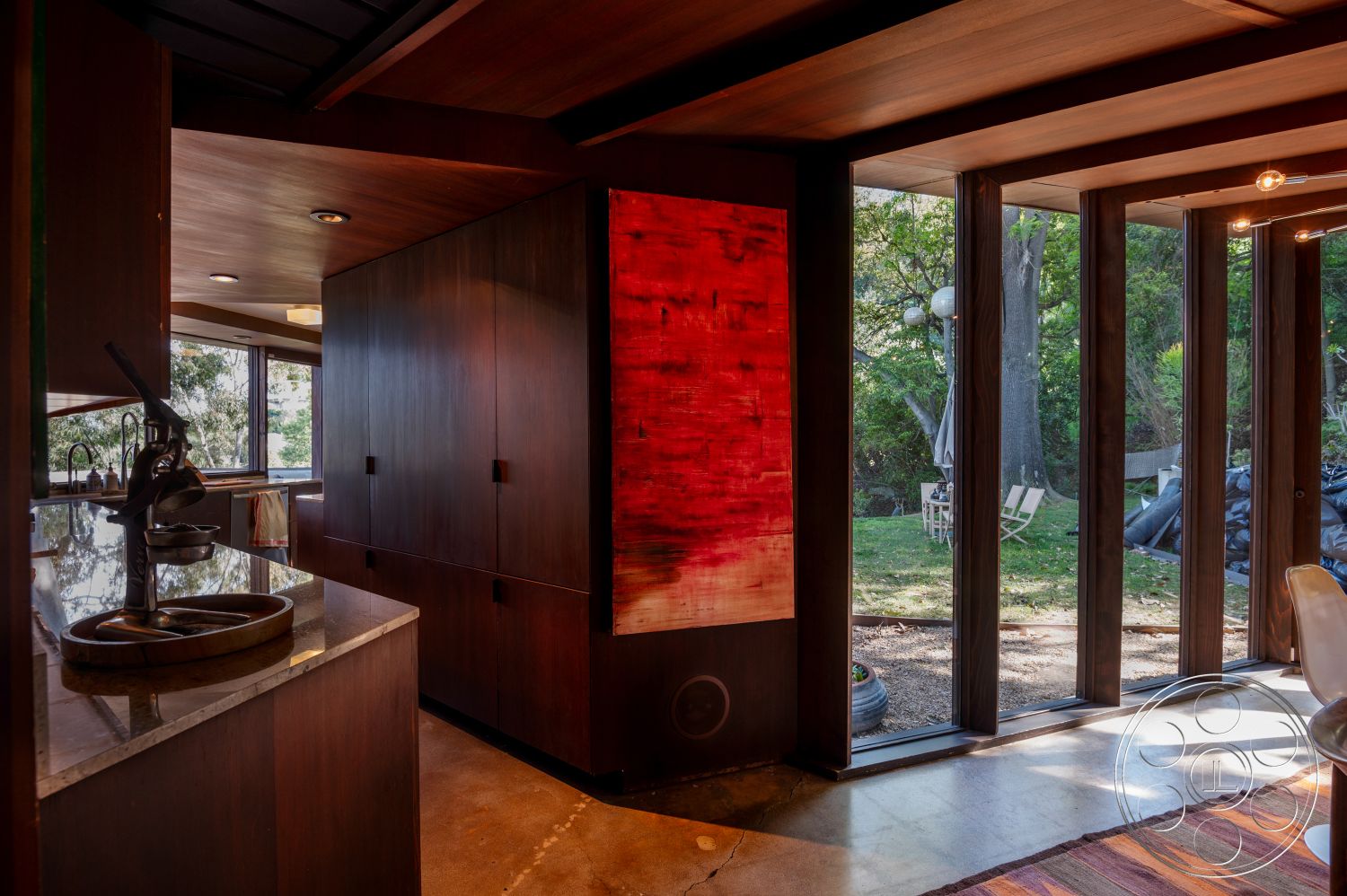 Retro 31 - interior textured plaster wall, interior natural light, exterior wood deck, interior chef's kitchen, interior wood beam ceiling, interior recessed lighting fixtures, exterior patio area, interior open-concept living space, interior modern aesthetic, exterior urban setting, interior glass window walls, interior walnut cabinetry, interior concrete kitchen floor, interior granite kitchen countertops, exterior landscaped backyard view, exterior natural surroundings, exterior eucalyptus trees backdrop