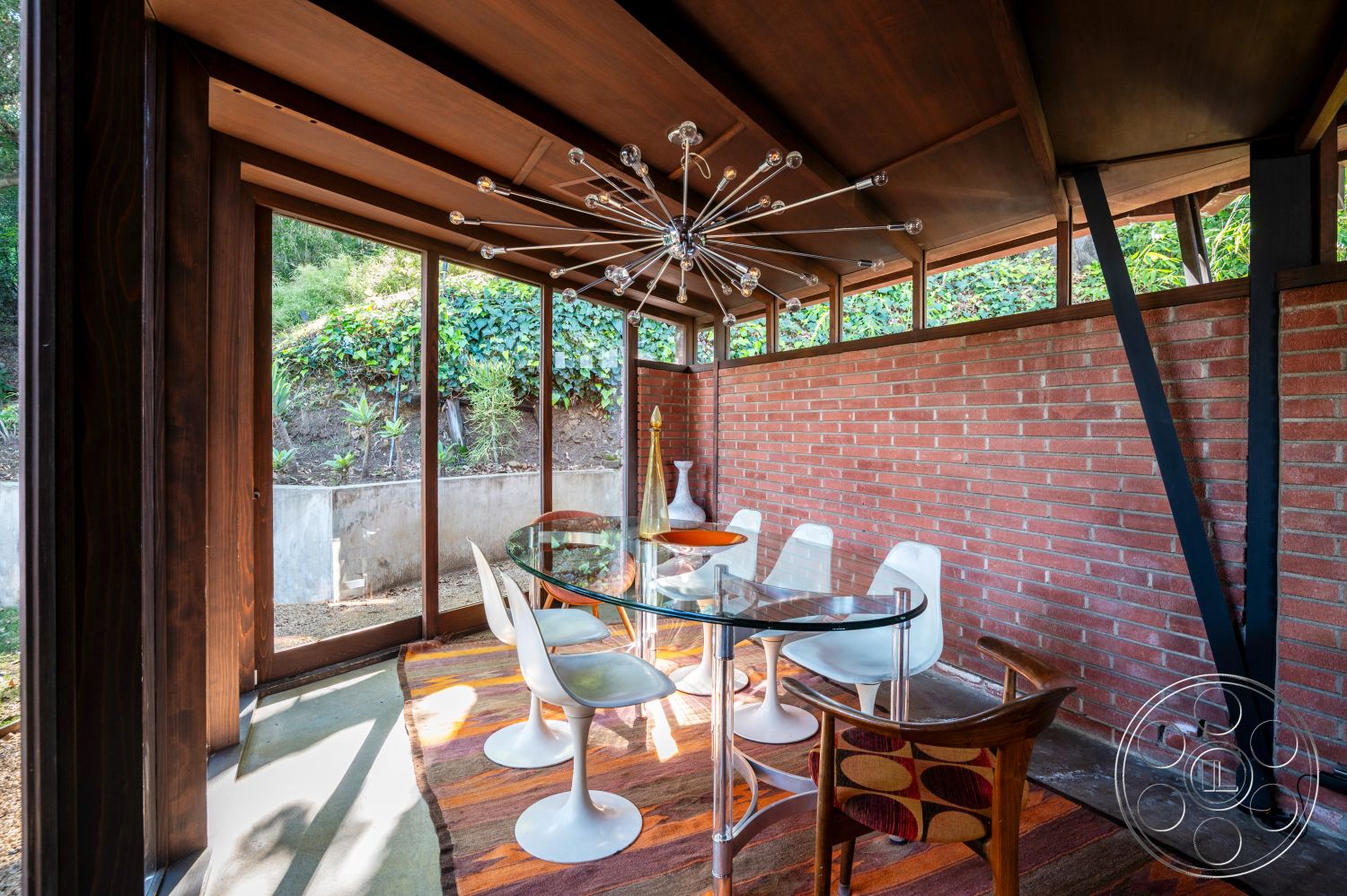 Retro 31 - polished concrete floor, floor-to-ceiling windows, glass dining table, open-concept layout, modern light fixture, lush greenery view, minimalist design aesthetic, wood beam ceiling, exposed brick accent wall, natural hillside setting, mid-century modern dining chairs, retro-inspired patterned chair
