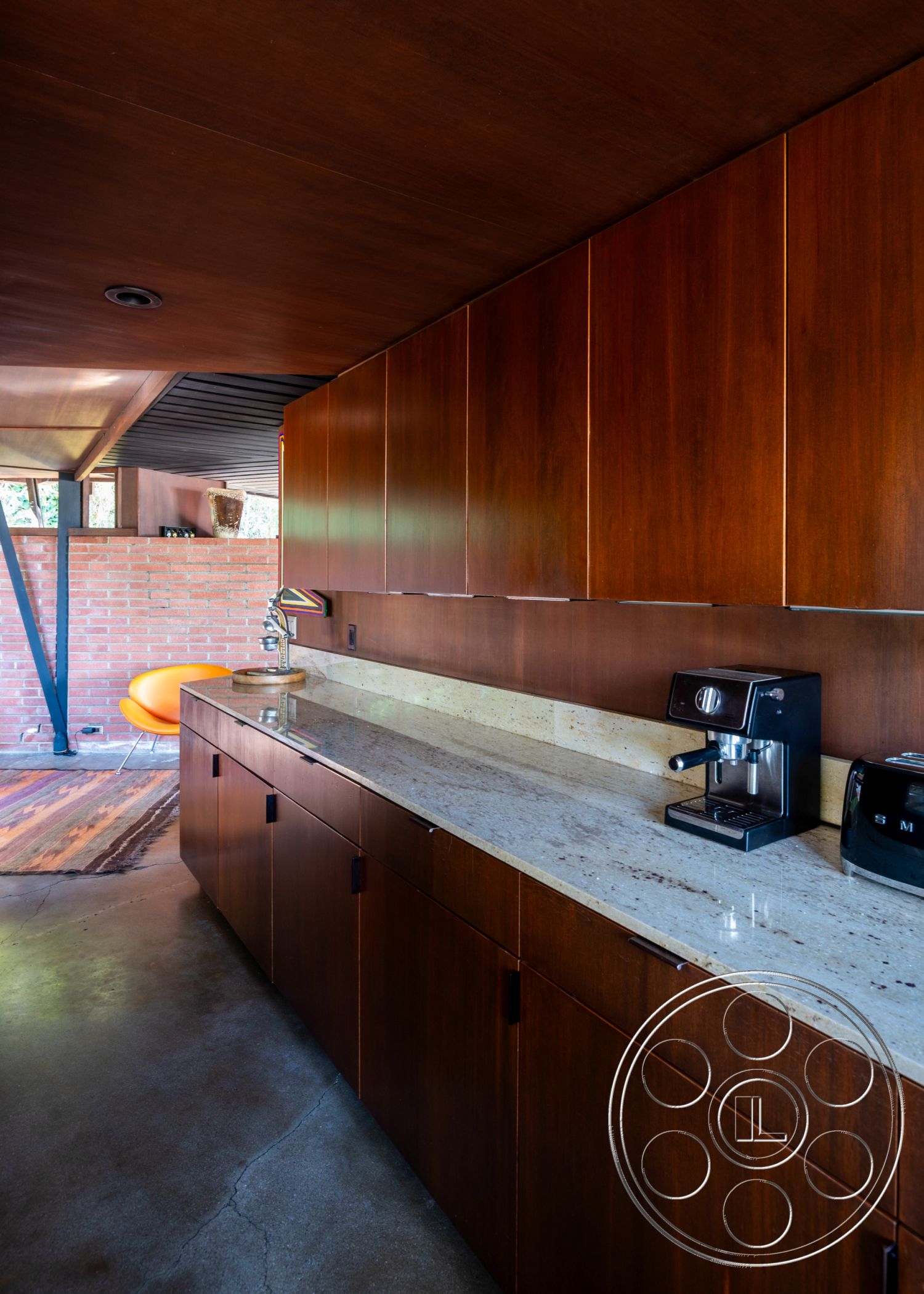 Retro 31 - textured area rug, stainless steel appliances, open-concept layout, under-cabinet lighting, pendant lighting fixtures, interior kitchen with walnut cabinetry, smooth wall surface, simple geometric shapes in design, concrete floor with polished finish, granite countertop with speckled pattern, exposed red brick accent wall, modern minimalist kitchen design, elegant coffee station, no-handle cabinet doors, mid-century modern chair