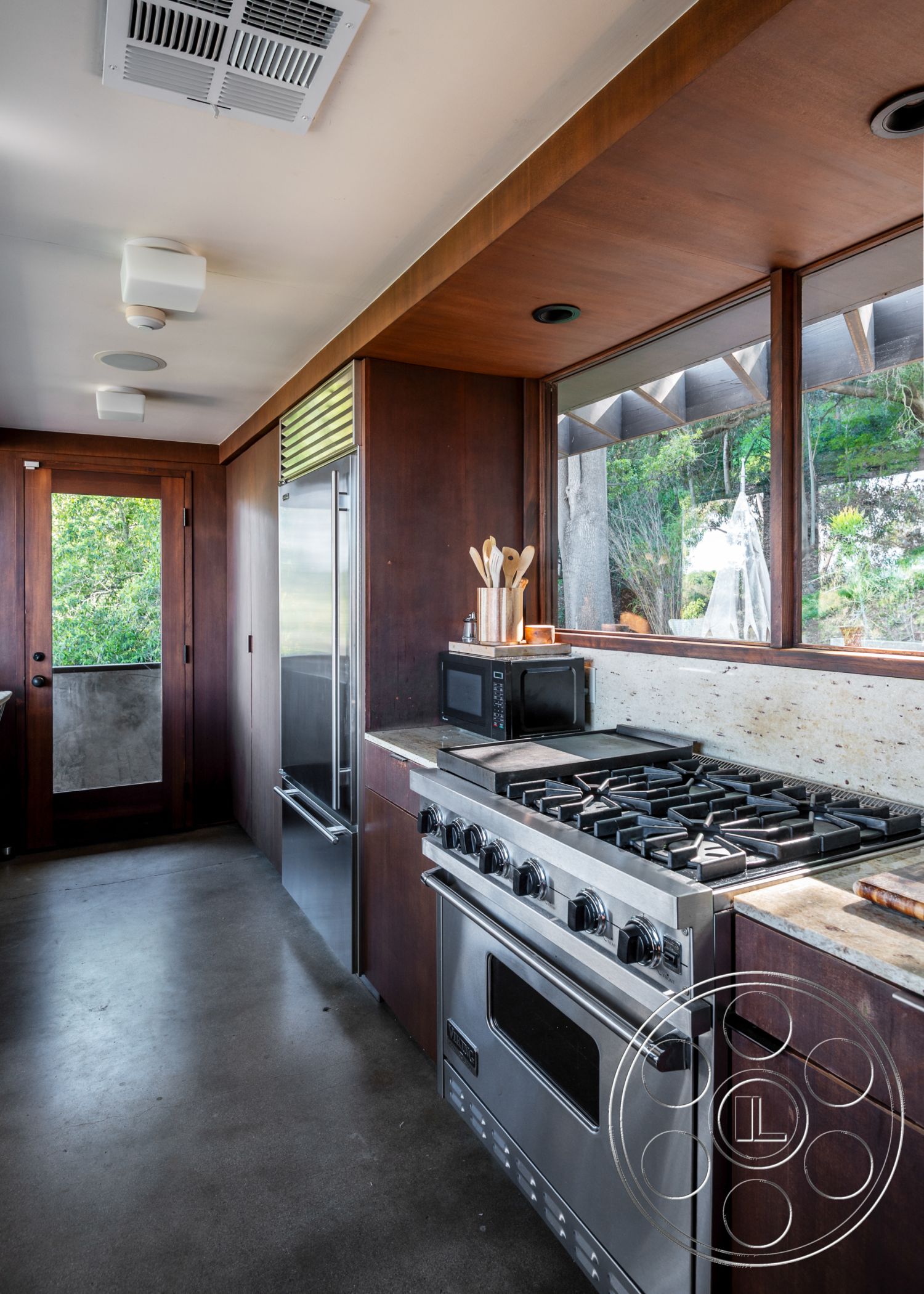 Retro 31 - neutral color palette, natural light, minimalist design, polished concrete floor, stainless steel appliances, wood cabinetry, open concept layout, modern pendant lighting, kitchen island, high ceiling, floor-to-ceiling windows, concrete countertop, sliding glass door, dark wood paneling, lush outdoor view, environmentally friendly design, textured backsplash, interior kitchen space, modern gas range