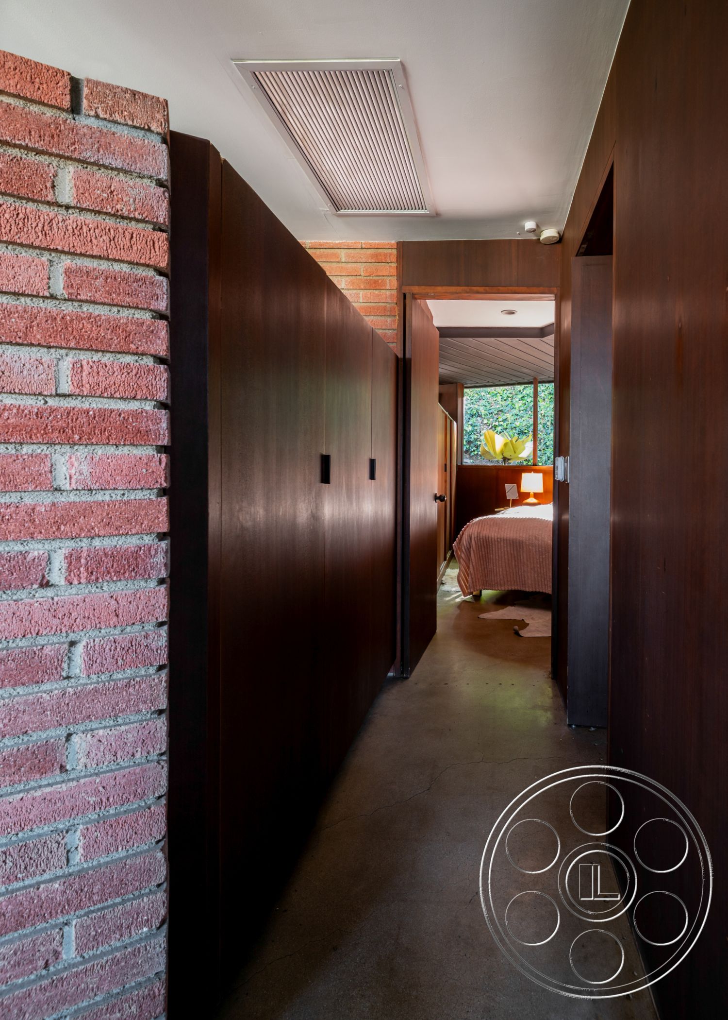 Retro 31 - serene atmosphere, concrete flooring, indoor-outdoor flow, ambient lighting features, textured wall finishes, dark wood paneling, open space concept, mid-century modern style, natural light interior, minimalist hallway design, modern architectural details, cohesive color palette, linear ceiling vents, exposed brick hallway wall, functional hallway layout, private bedroom access, garden views from hallway