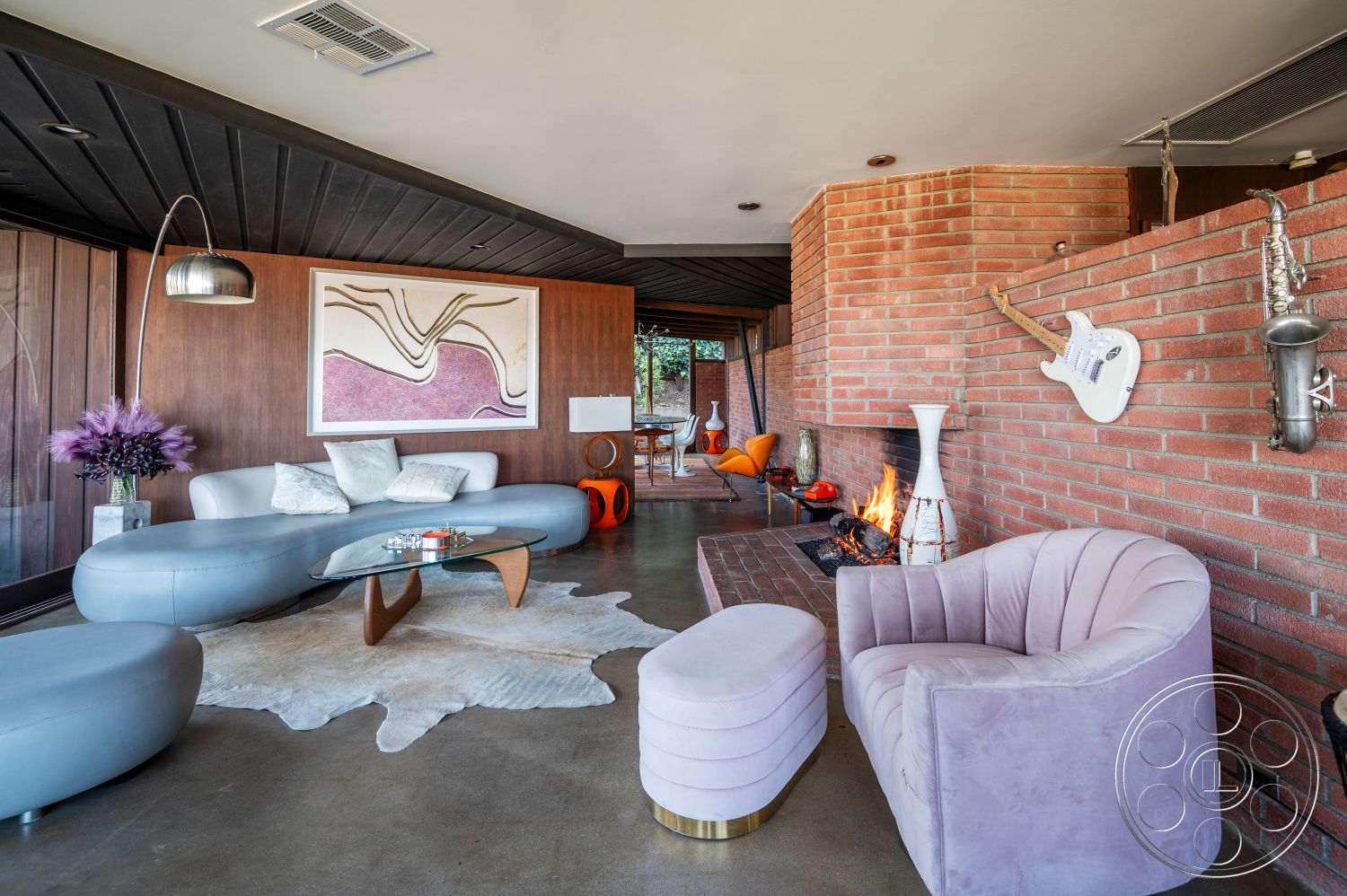 Retro 31 - interior polished concrete flooring, interior exposed brick accent wall, interior mid-century modern decor, interior low-profile curved sofas, interior playful modern armchairs, interior glass coffee table with wooden base, interior decorative wall art with abstract design, interior modern floor lamp with metallic finish, interior wood paneling on walls, interior sleek white fireplace surround, interior cozy fireplace with stacked firewood, interior animal-skin rug, interior round pink velvet accent chair, interior small pink ottoman, interior sunny indoor space with large windows