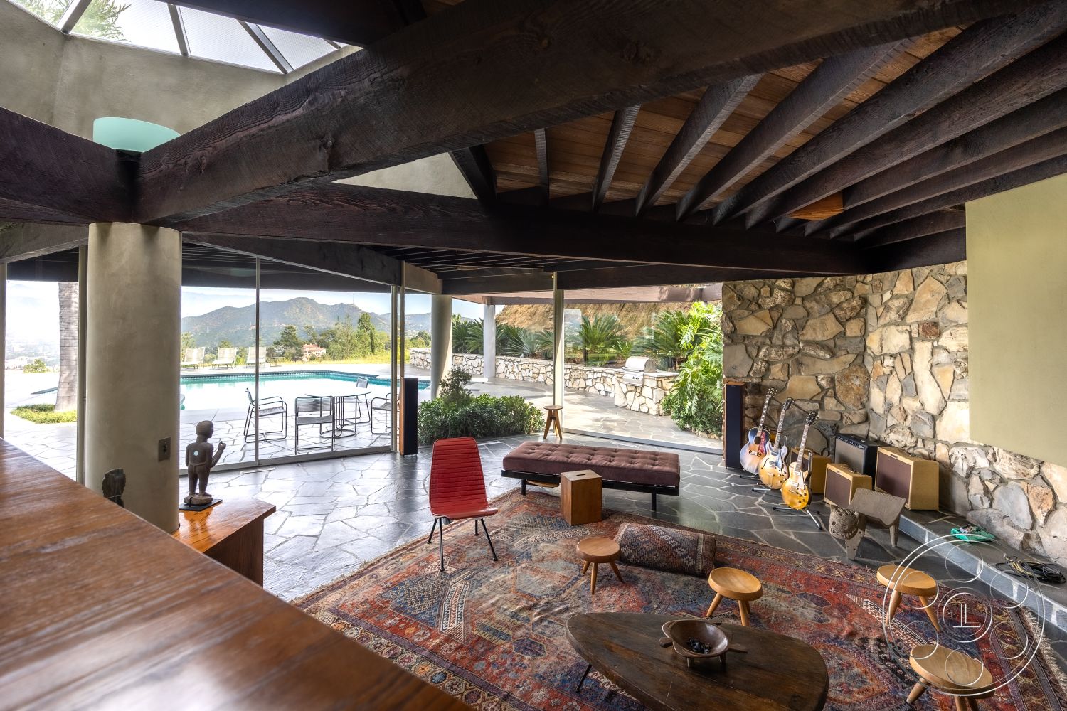 Retro 19 - wooden coffee table, landscaped garden view, rectangular swimming pool, open concept living room, casual seating arrangement, exposed wood ceiling beams, mid-century modern architectural style, minimalist interior design, floor-to-ceiling glass doors, slate patio flooring, natural stone feature wall, textured plaster interior walls, large panoramic windows, exterior swimming pool area, rustic area rug, glass wall openings, hardwood furniture accents, desert hillside location, built-in music equipment corner, outdoor patio seating