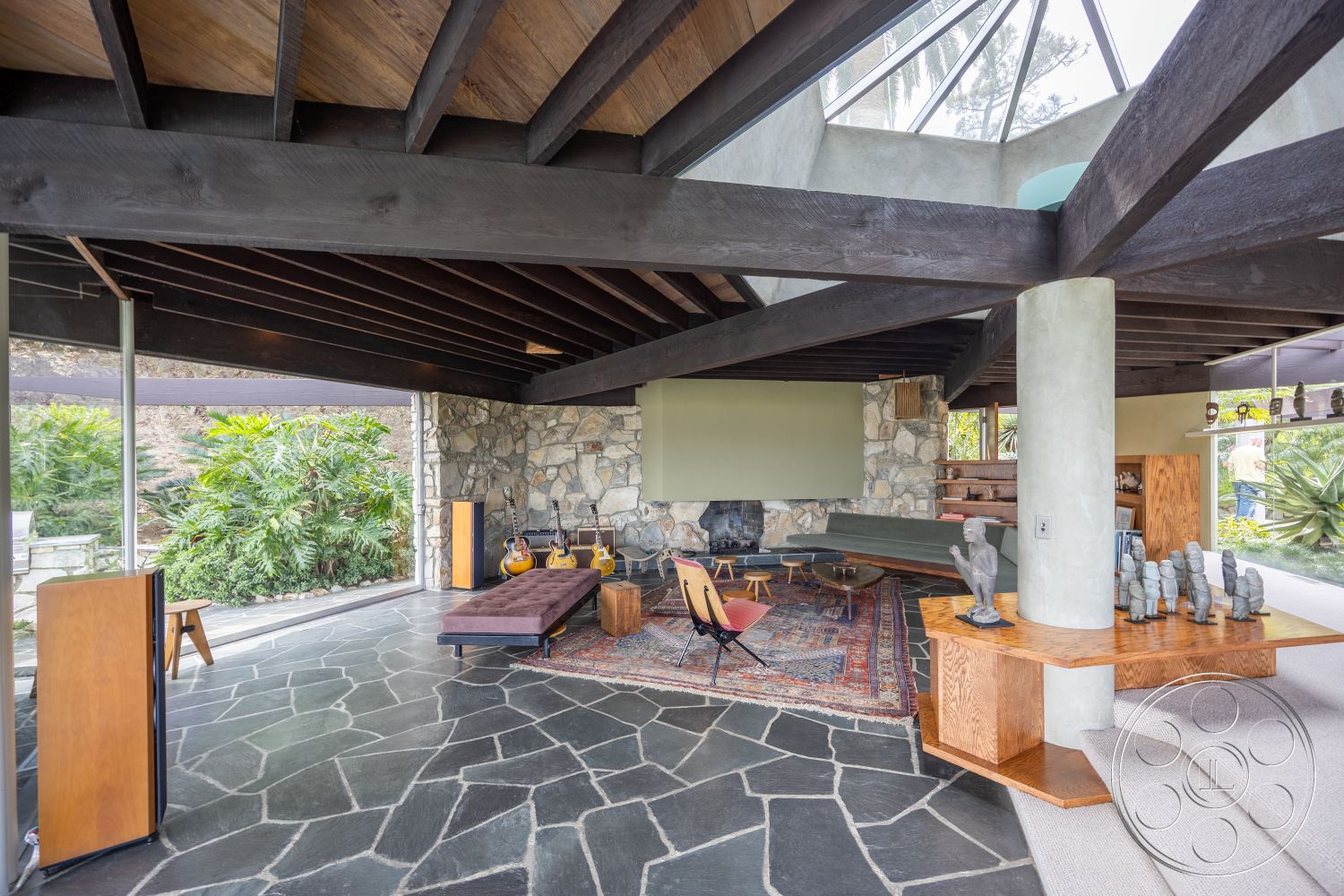 Retro 19 - mid-century modern architectural style, exposed wood ceiling beams interior, floor-to-ceiling windows interior, modern fireplace feature interior, wooden coffee table interior, earthy color palette interior, modern wood furniture interior, slate stone flooring interior, natural stone accent wall interior, concrete support columns interior, large glass skylight interior, contemporary rug interior, open-space layout interior, modern art sculptures interior, lush green landscaping exterior, outdoor seating area exterior, palm tree setting exterior, wood paneled accent wall interior, recessed lighting interior