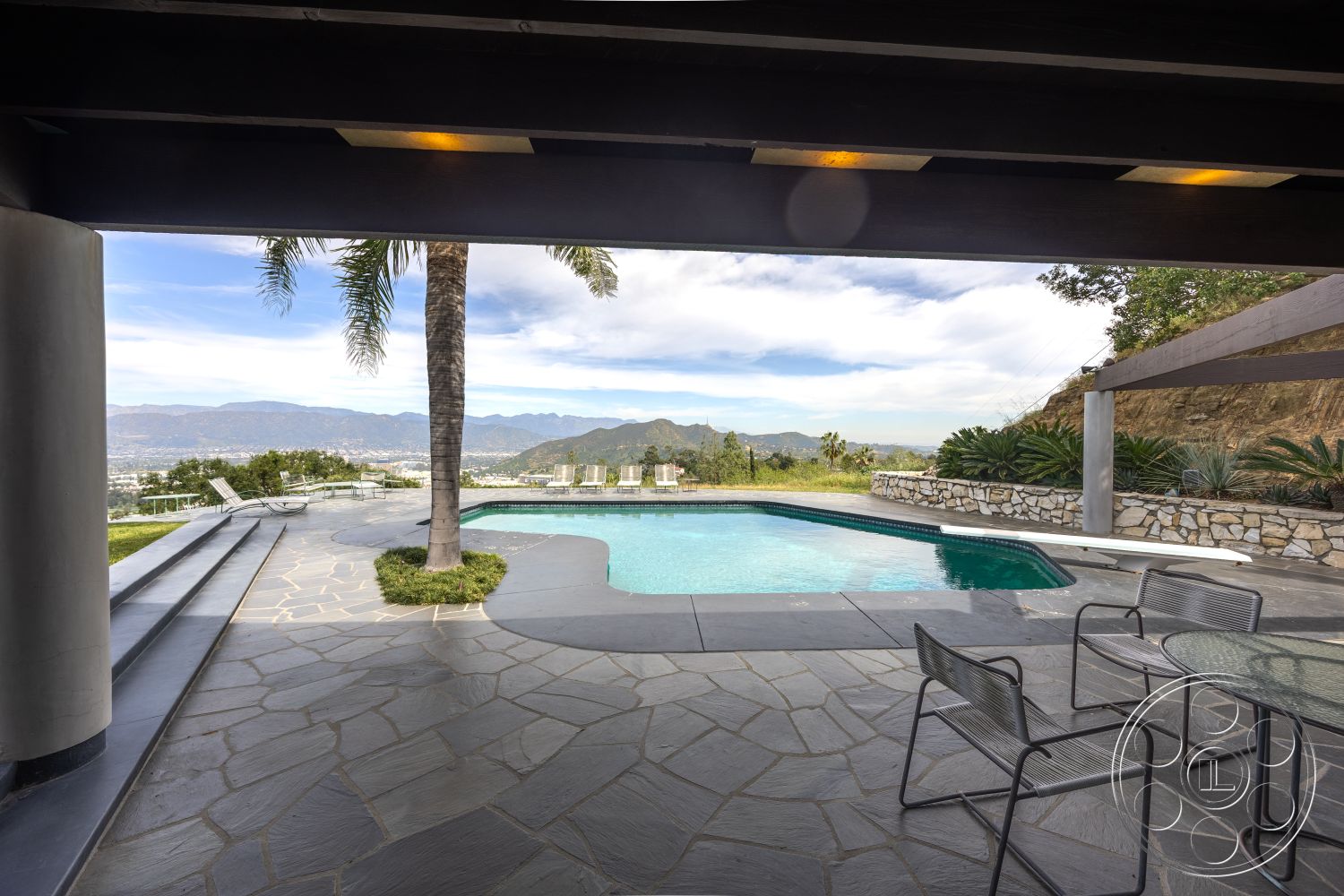 Retro 19 - exterior, rectangular swimming pool, concrete steps, metal outdoor furniture, natural stone retaining wall, mountain view setting, landscaped garden area, patio dining area, palm trees landscape, open sky view, spacious outdoor living space, modern outdoor architecture, hardscaped patio area, slate stone pool deck, exposed wood overhang, stainless steel pool ladder