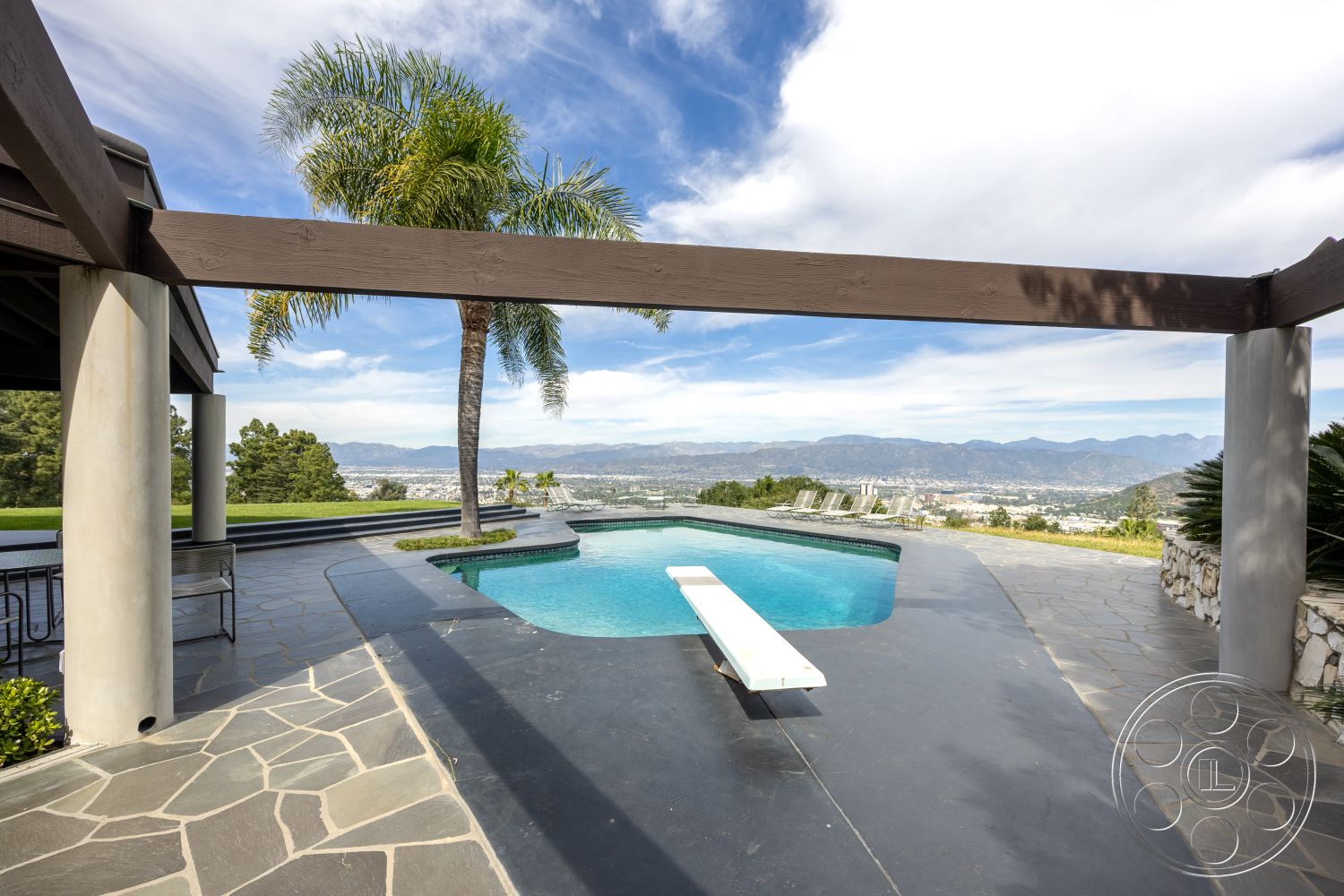 Retro 19 - modern outdoor furniture, rectangular swimming pool, outdoor lounge area, concrete patio floor, landscaped hillside view, covered outdoor dining space, tiled pool coping, exposed wood pergola, slate stone pool deck, mountain skyline backdrop, pillared patio structure, lush palm tree landscaping, light gray stone pavers, interior and exterior transition