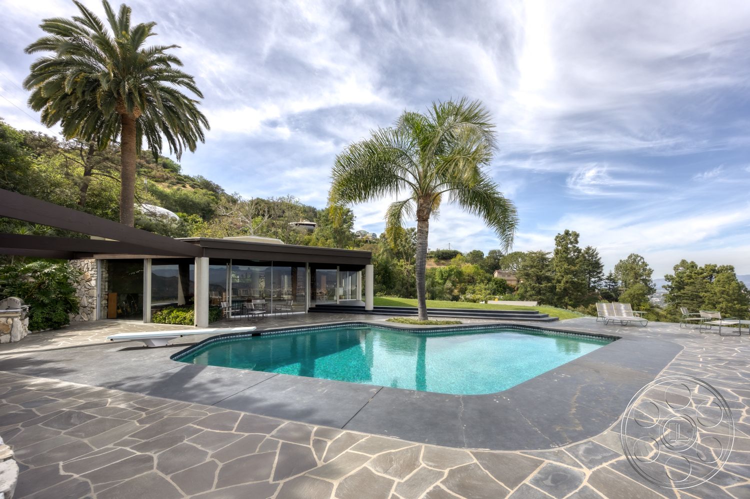 Retro 19 - exterior, modern architectural style, open concept living space, flat roof design, landscaped garden setting, concrete pool border, poolside palm trees, natural stone patio flooring, mountain view backdrop, slate stone pool deck, rectangular pool with built-in spa, glass walls for poolside view, metal shade structure, outdoor lounging area with chairs, lawn area for activities