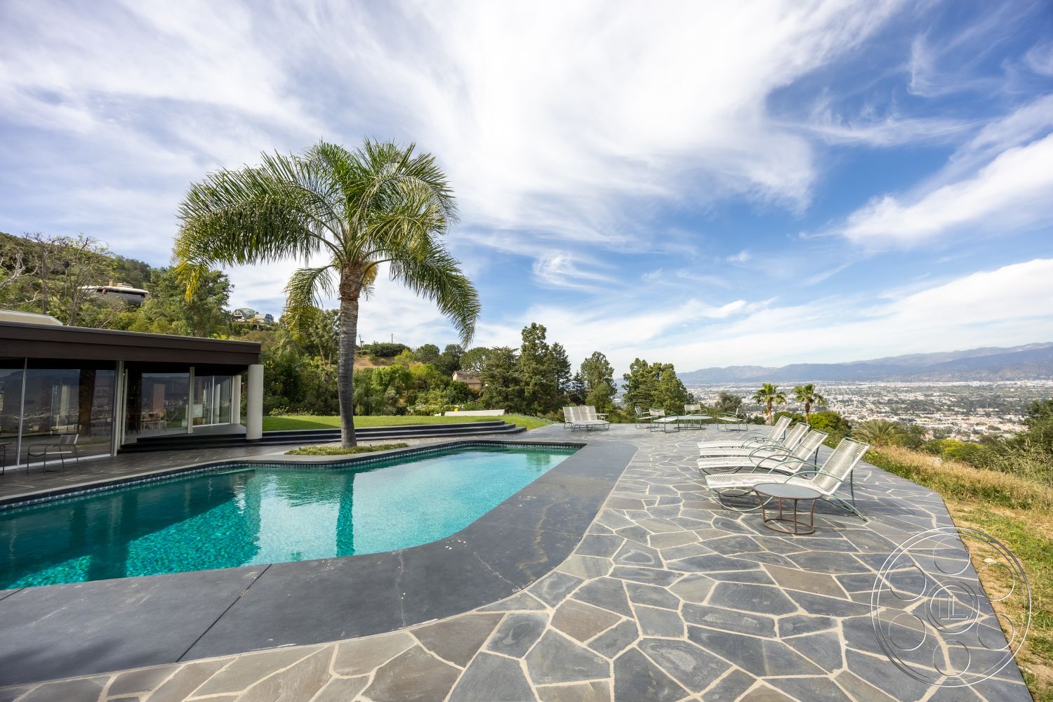 Retro 19 - modern architectural style, exterior seating area, rectangular pool, stone pool deck, landscaped garden setting, glass wall panels, luxury outdoor living space, slate patio flooring, mountain view backdrop, infinity pool edge, aluminum lounge chairs, open-air poolside environment
