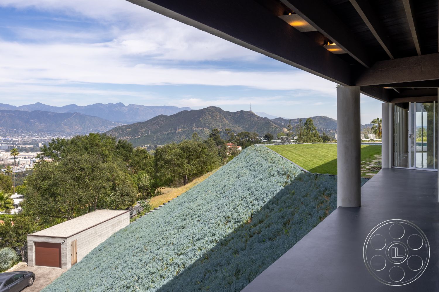 Retro 19 - large glass windows, glass sliding doors, exterior view, modern architectural style, hillside location, flat roof design, exposed wood ceiling beams, concrete patio floor, landscaped hillside garden, urban modern home, mountain landscape backdrop, natural light-focused design, cantilevered roof structure, concrete garage structure, greenery around home, minimalist outdoor area