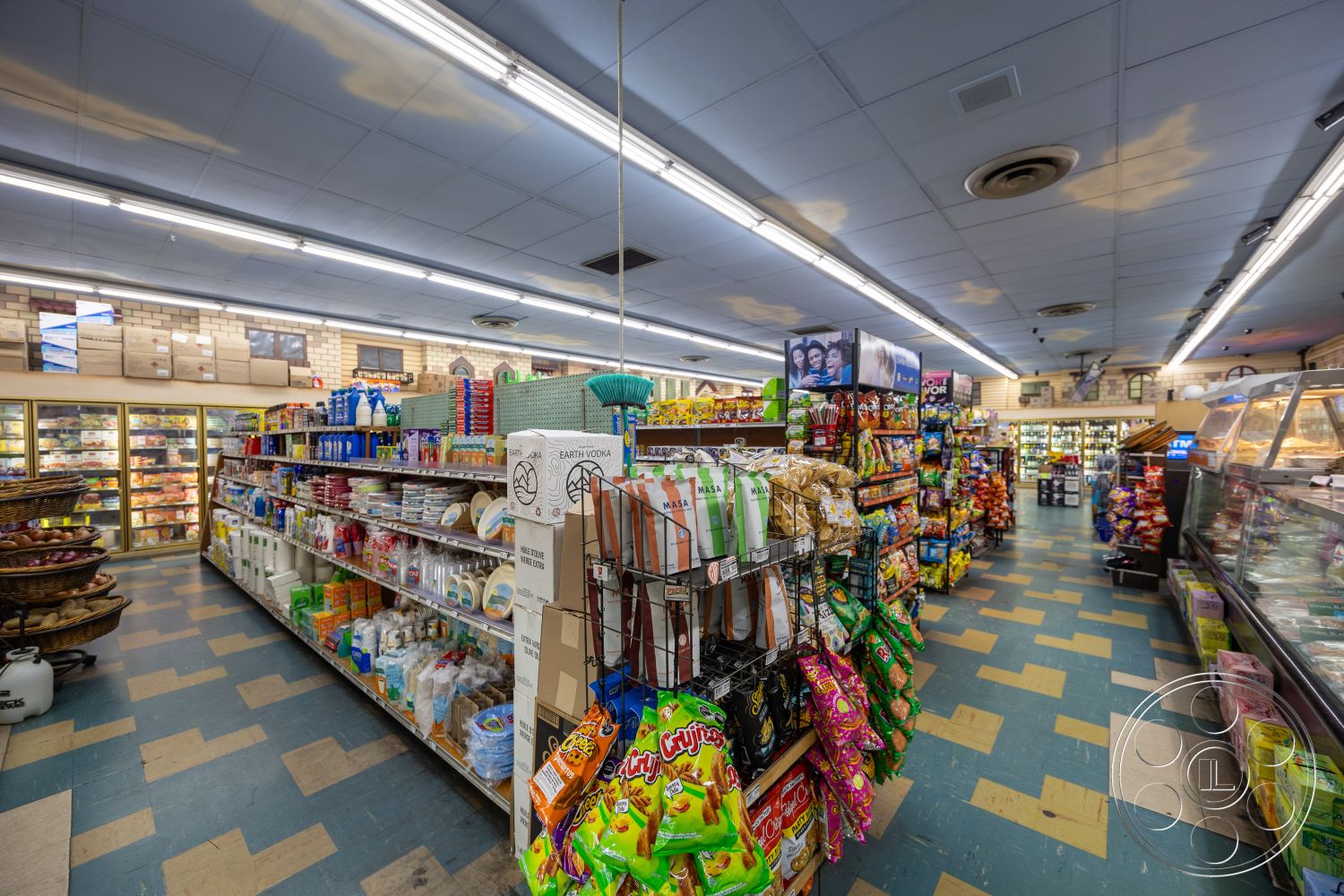 Shop 128 - metal shelving units, brick wall accents, glass display cases, exposed ceiling tiles, fluorescent ceiling lights, snack food displays, blue and beige vinyl flooring, packaged goods on shelves, grocery aisle layout