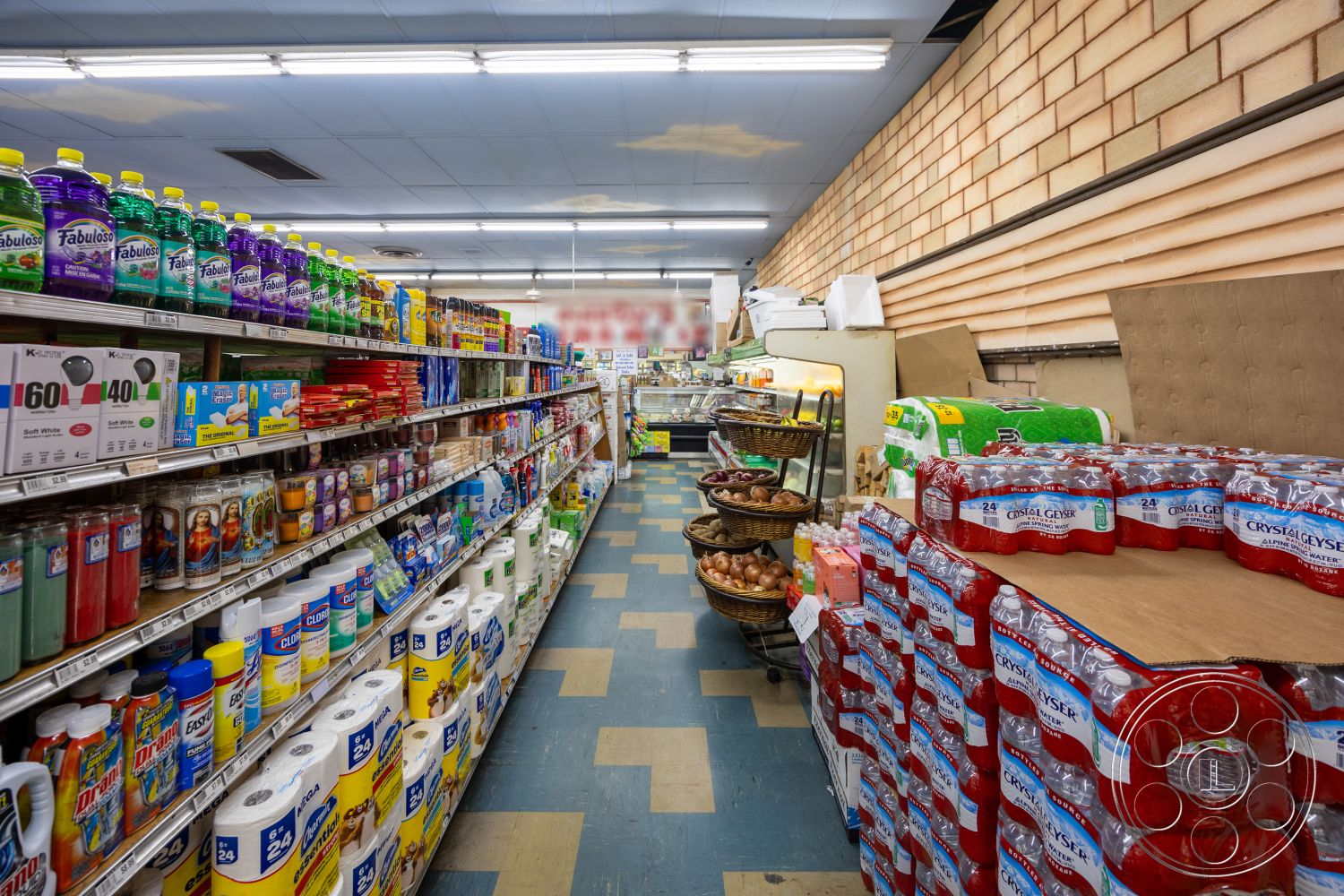 Shop 128 - metal shelving units, exposed brick wall, bright fluorescent lighting, linoleum flooring, variety of consumer goods, aisle shelving, plastic product containers, basket display stands, long narrow aisle layout