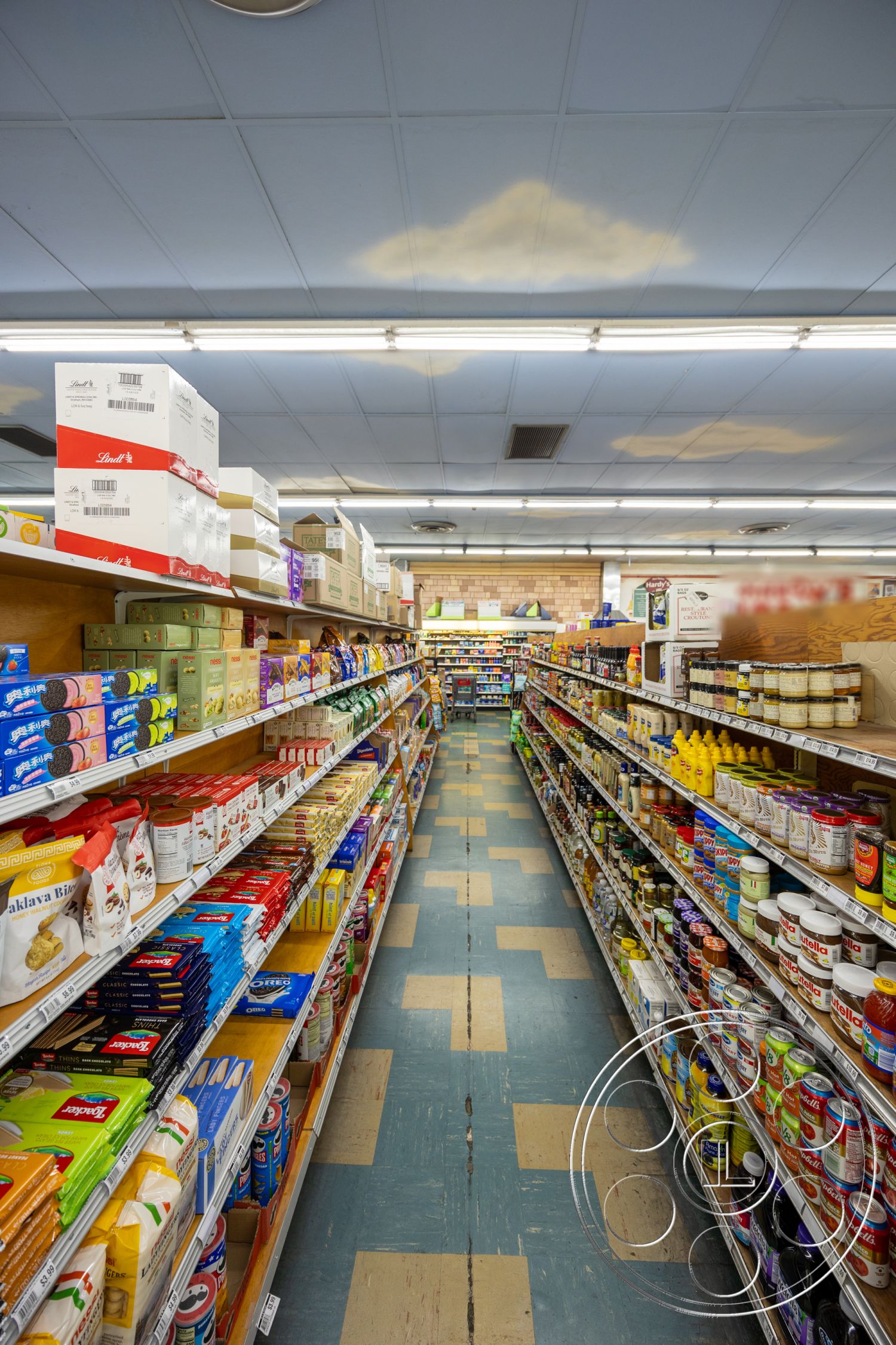 Shop 128 - wooden shelving units, overhead fluorescent lighting, vinyl flooring with checkerboard pattern, blue ceiling tiles, shelves stocked with various food products, aisle layout for grocery store, boxed food products, packaged snacks display