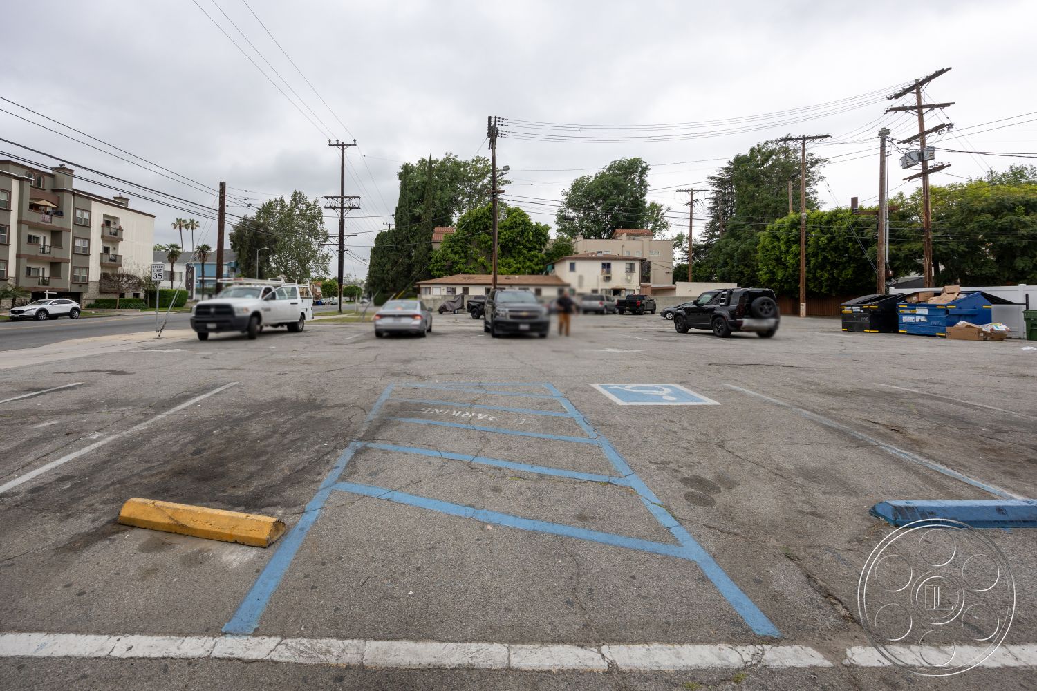 Shop 128 - urban setting, landscaped trees, utility poles, asphalt parking lot, striped parking spaces, cloudy sky, concrete curb, residential building exterior, dumpster area, interior parking lot