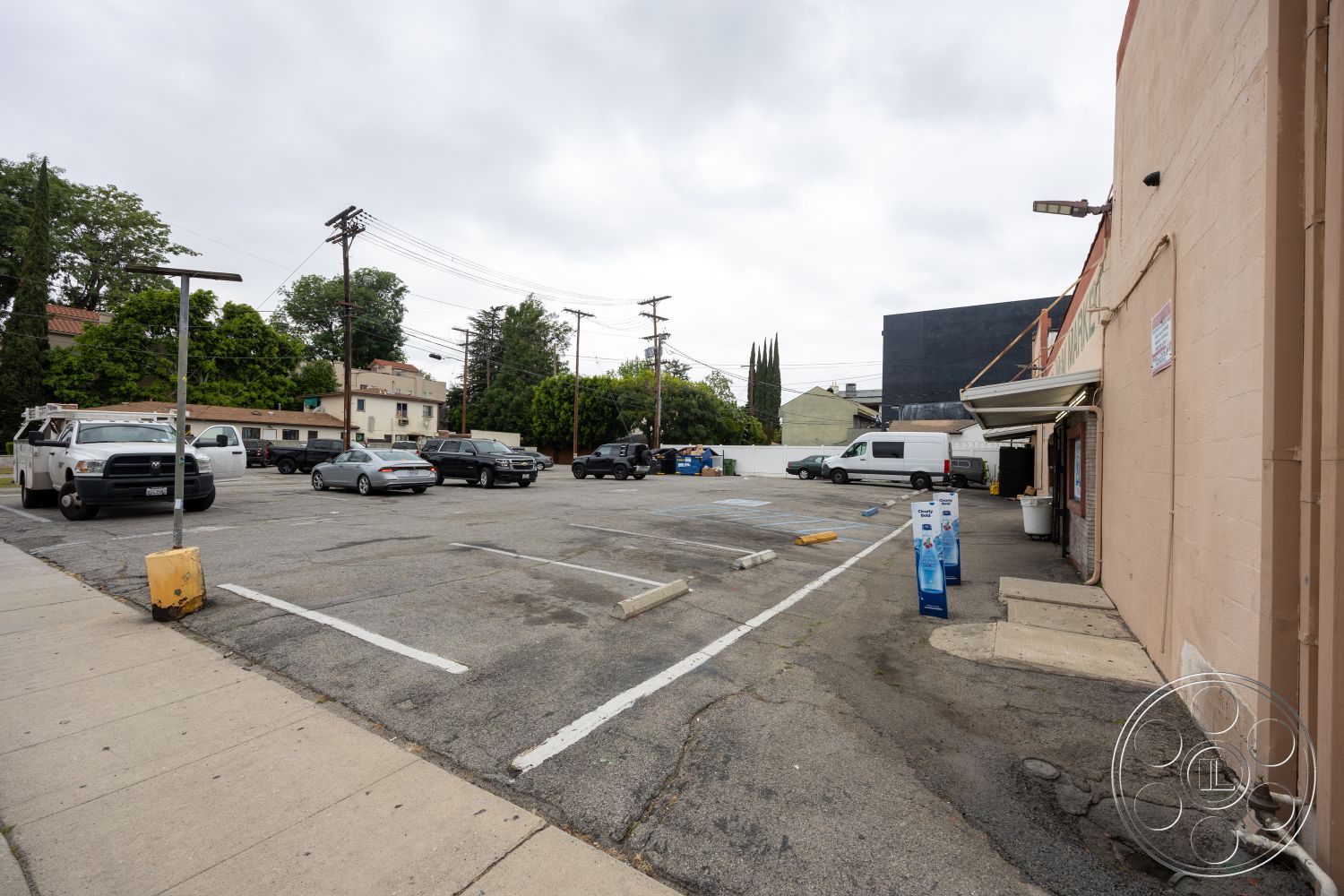 Shop 128 - exterior, asphalt surface, urban setting, utility poles, block wall, paved parking lot, storage bins, single-story commercial building, concrete curb, landscaped area with trees, painted stucco walls, vehicles in parking spaces