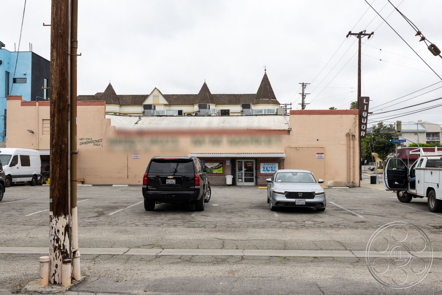Shop 128 - exterior, flat roof, asphalt parking lot, overhead power lines, modern geometric shapes, multi-story residential building, painted brick facade, metal store sign, wood utility pole, parking space markings, partial storefront windows