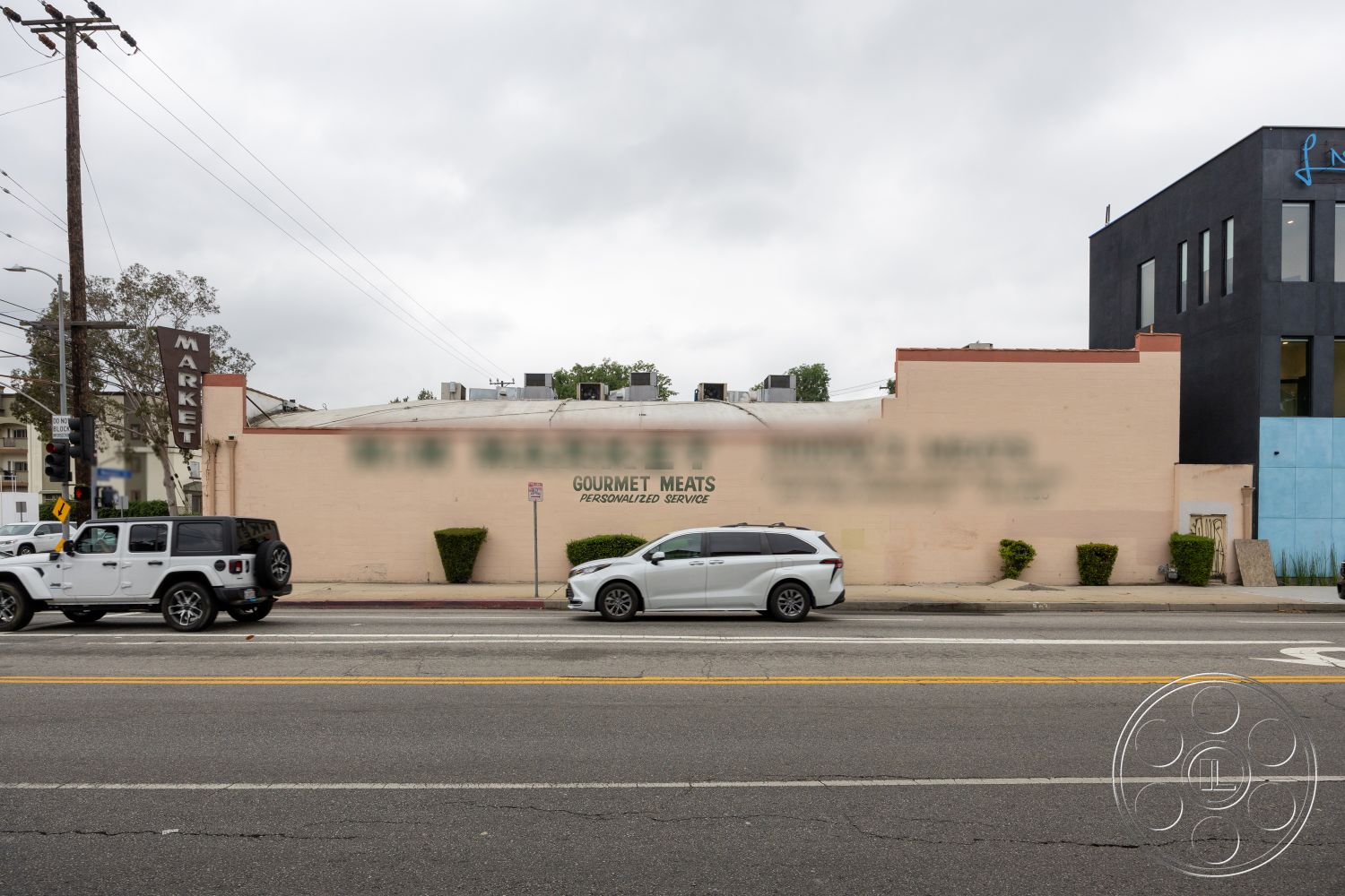 Shop 128 - exterior, flat roof, power lines, stucco wall finish, landscaped shrubbery, urban commercial setting, rectangular building shape, asphalt roadway, parking lot surface, signage for market, modern building adjacent, cloudy sky atmosphere