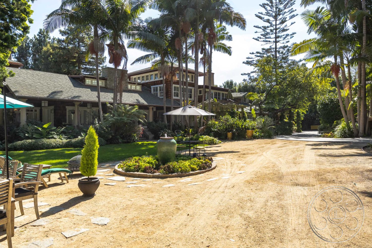 Americana 48 - exterior, landscaped garden, palm trees, natural wood accents, tropical plants, stone pathway, circular flower bed, poolside lounge area, shingle roof, two-story home, outdoor umbrella, modern house, wood panel siding, hardwood patio seating, in-ground flower planters, sand driveway