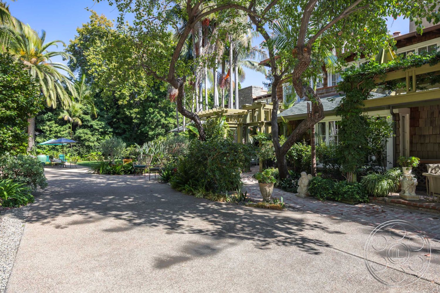 Americana 48 - large windows, exterior, landscaped garden, lush greenery, palm trees, brick walkway, open courtyard, concrete driveway, wooden pergola, suburban backyard, garden seating area, patio umbrella, sloped roof design, stone garden planters, wood shingle exterior