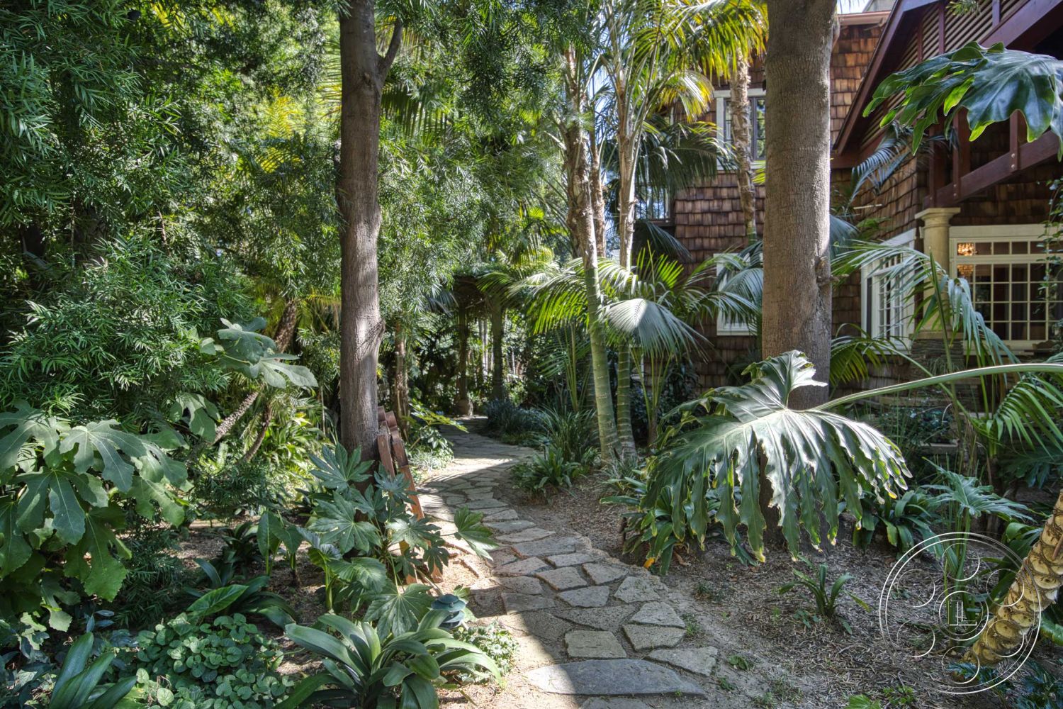 Americana 48 - exterior, lush greenery, palm trees, curved pathway, stone pathway, tropical landscaping, dappled sunlight, dense foliage, bamboo accents, natural stone borders, wood shingle house facade