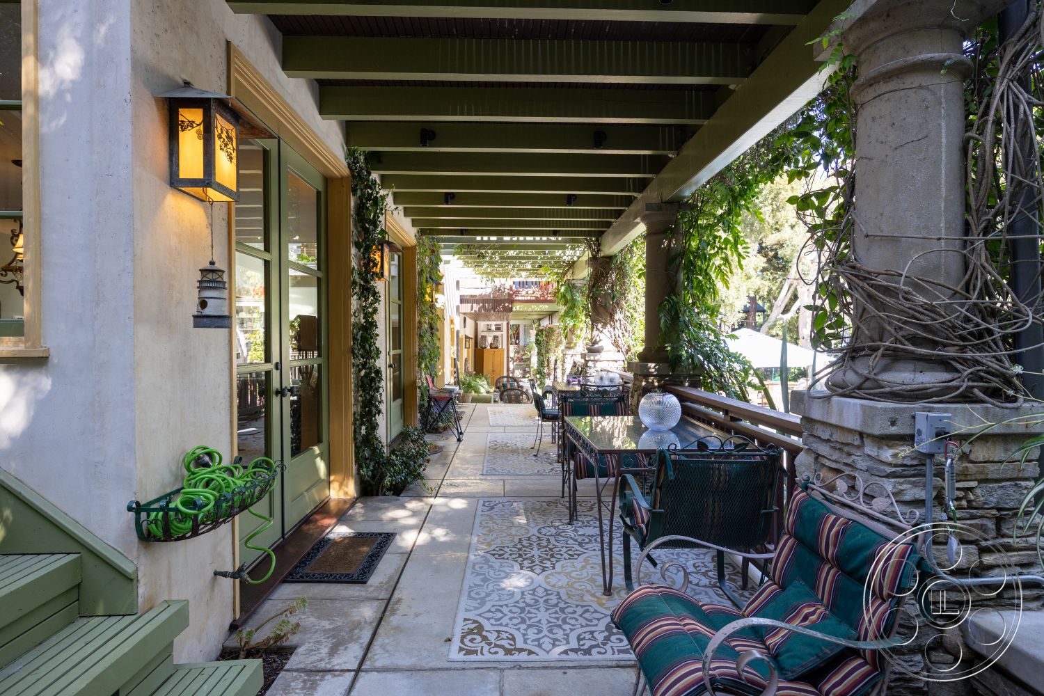 Americana 48 - exterior, outdoor seating area, wood beam ceiling, textured concrete walkway, green ivy wall treatment, green painted wooden steps, exposed stone columns, wrought iron patio furniture, decorative ceramic tiles, lantern style lighting fixture