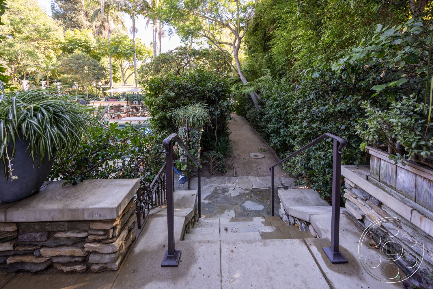 Americana 48 - lush greenery, outdoor seating area, exterior landscaping, concrete steps, cobblestone pathway, metal handrails, stone step pathway, planter with ornamental grass, wooden fence accent, interior transition from garden to poolside