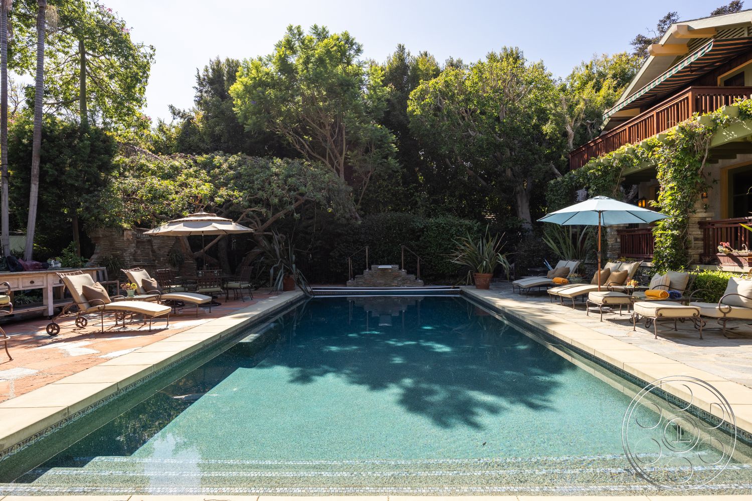 Americana 48 - natural light, exterior, landscaped garden, lush greenery, private backyard, relaxation area, rectangular pool, outdoor umbrellas, stone patio flooring, concrete pool border, wooden sun loungers, brick outdoor wall, staircase to pool area, southwestern setting