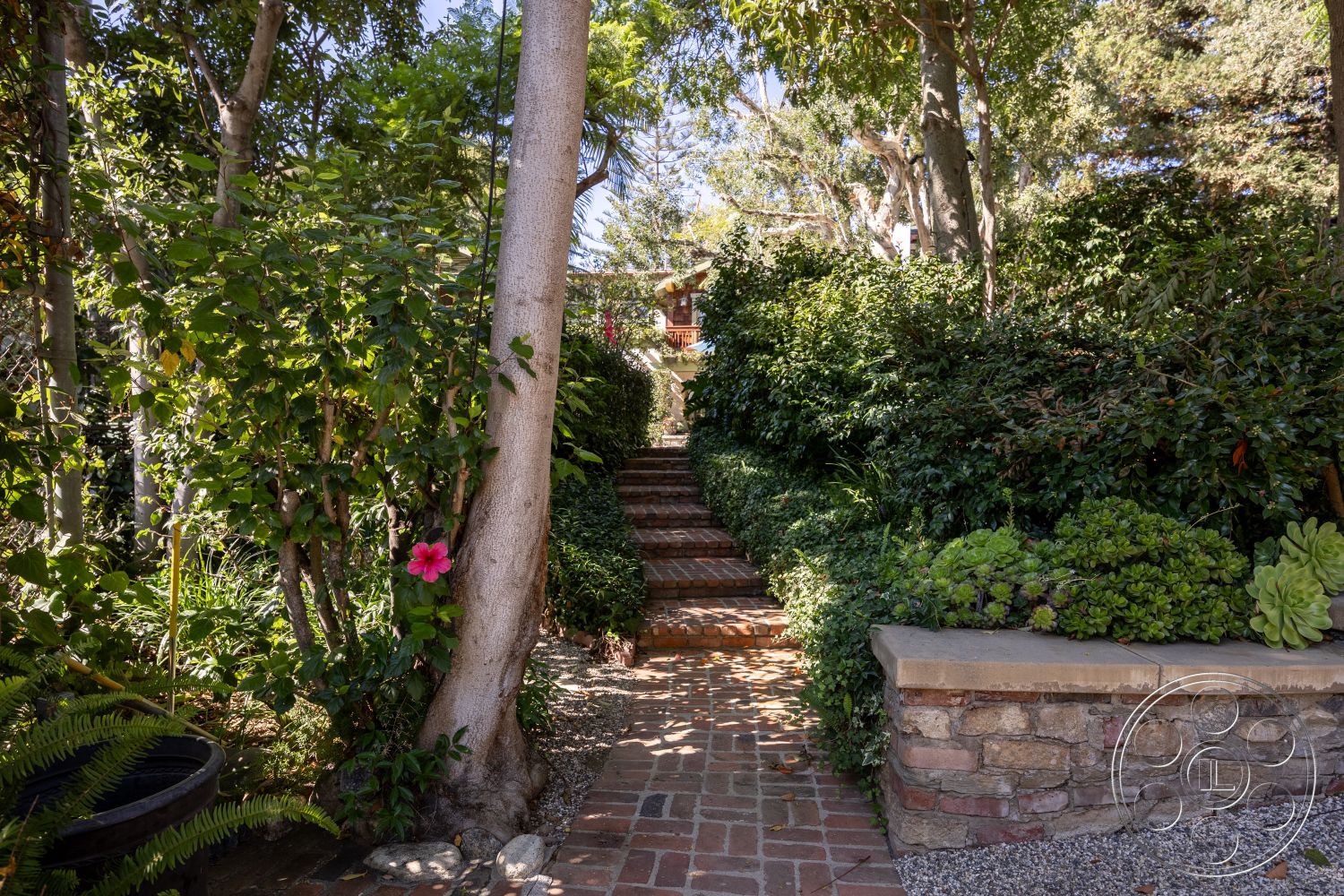 Americana 48 - landscaped garden, lush greenery, brick pathway, flowering plants, stone retaining wall, interior garden setting, steps leading to home, wooden deck overlooking garden
