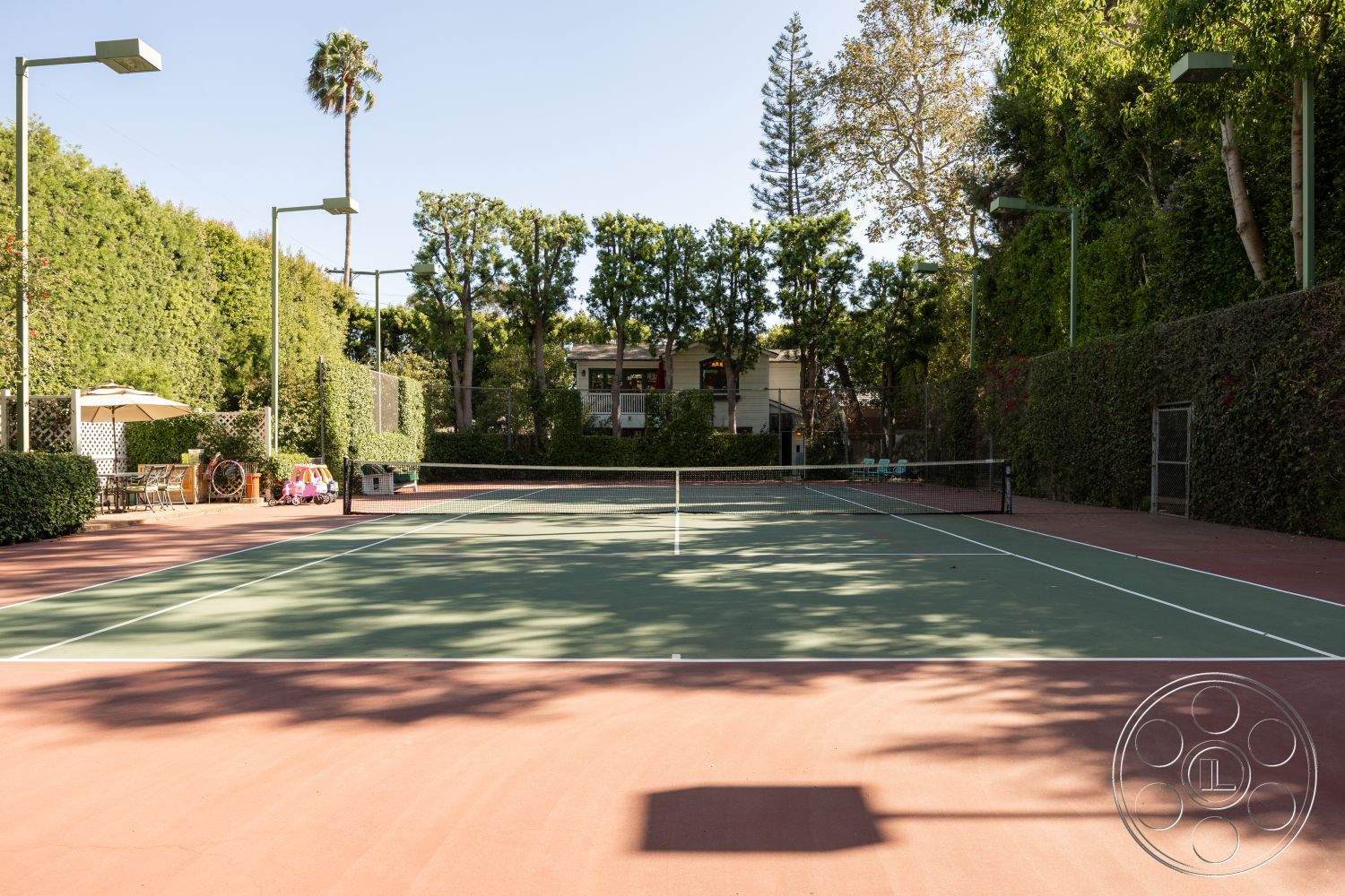 Americana 48 - surrounding trees, landscaped hedges, wooden deck area, exterior lighting fixtures, residential backyard setting, tennis court surface, red clay tennis court, green acrylic tennis court, outdoor patio with umbrella, metal tennis court net posts, contemporary tennis court design