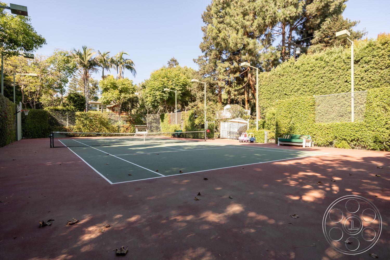Americana 48 - wooden bench seating, outdoor lighting fixtures, sunny outdoor setting, exterior tennis court surface, hard court tennis court, surrounding lush landscaping, fenced tennis court area, concrete tennis court border, green tennis net, hedge privacy walls, paved court area