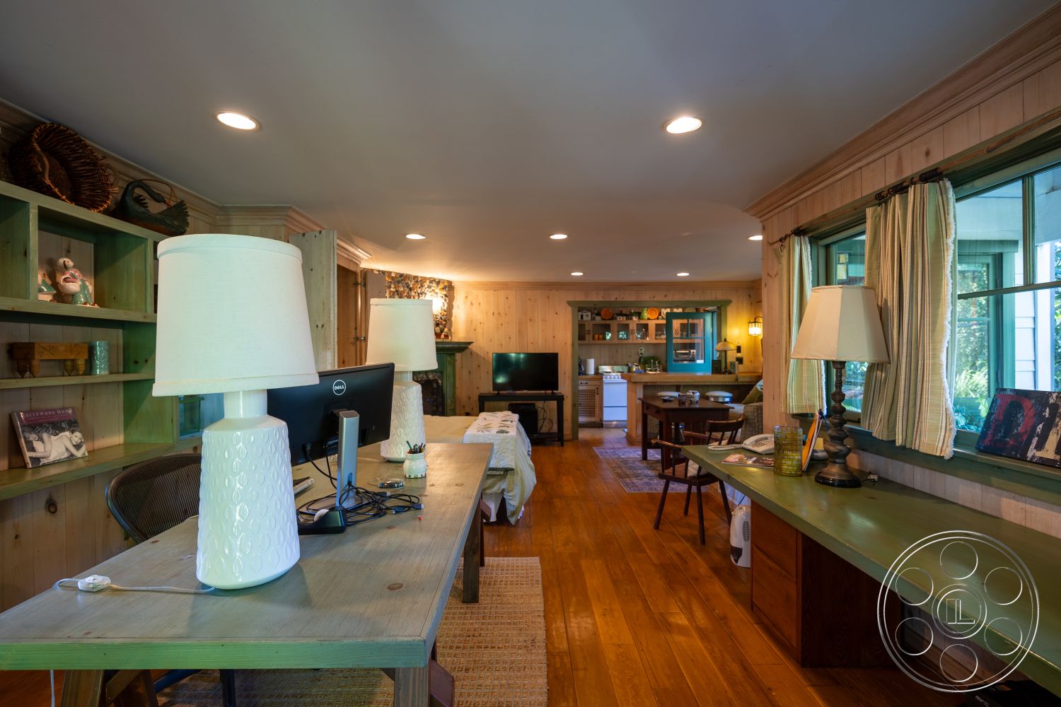 Americana 48 - large windows, open floor plan, hardwood floor, built-in bookshelf, comfortable seating area, wood paneling walls, contemporary desk lamp, traditional dining table, green accent cabinetry, kitchen area with appliances